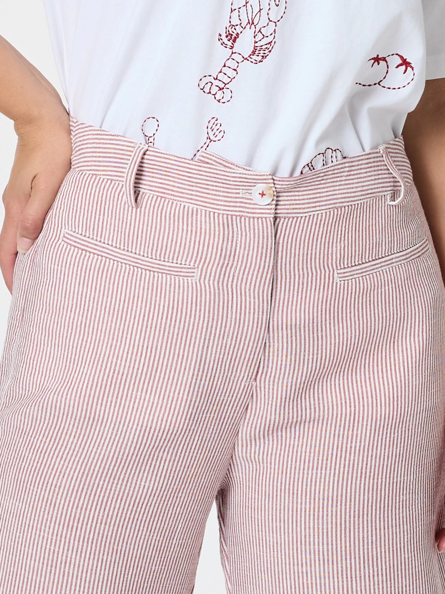 Image of Close-up of a woman wearing Threadz pink and white vertically striped trousers with a white embroidered T-shirt tucked in.