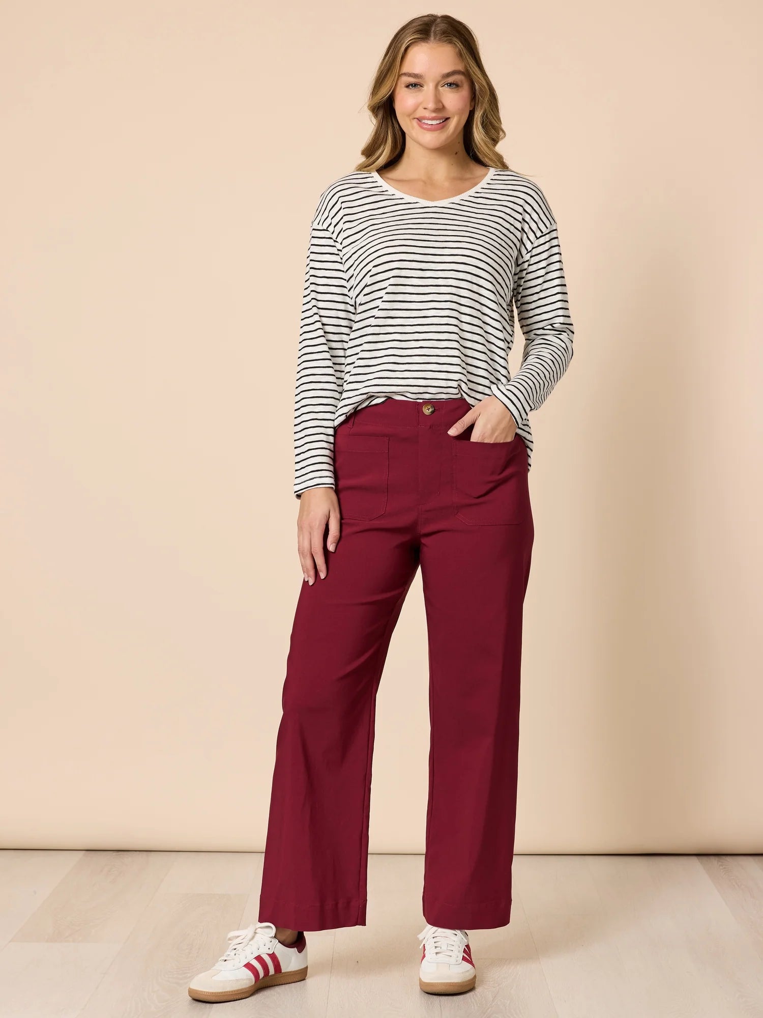 Image of Woman wearing a Threadz striped shirt and burgundy pants against a beige background