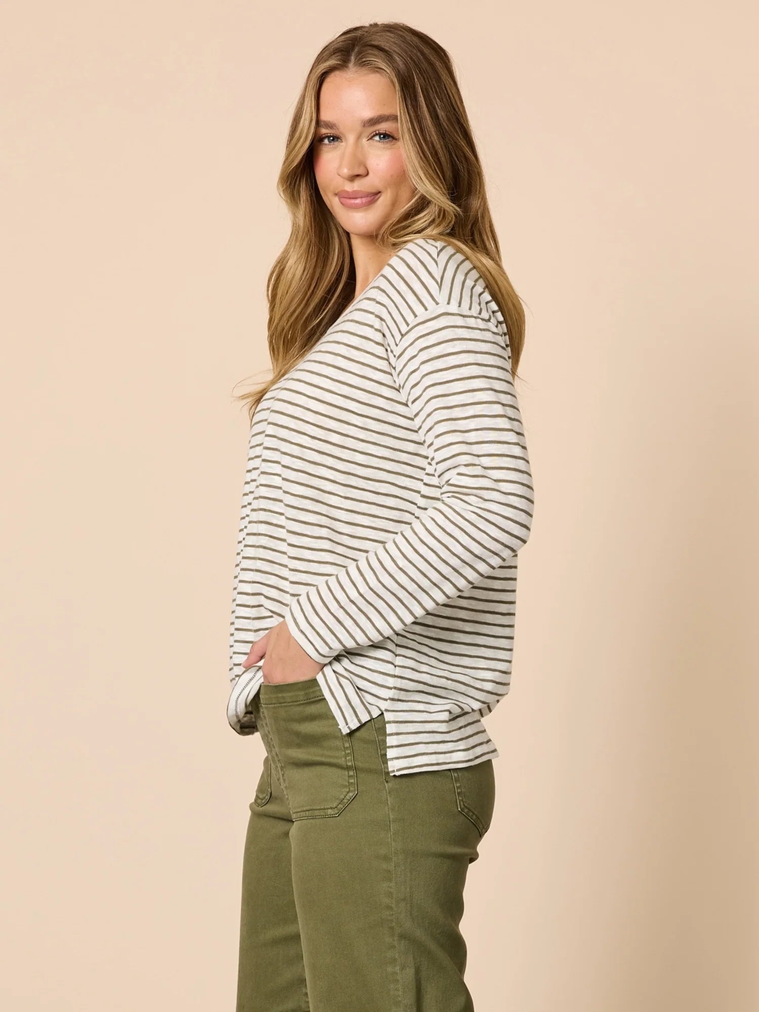 Image of Woman wearing a Threadz striped sweater and green pants against a beige background