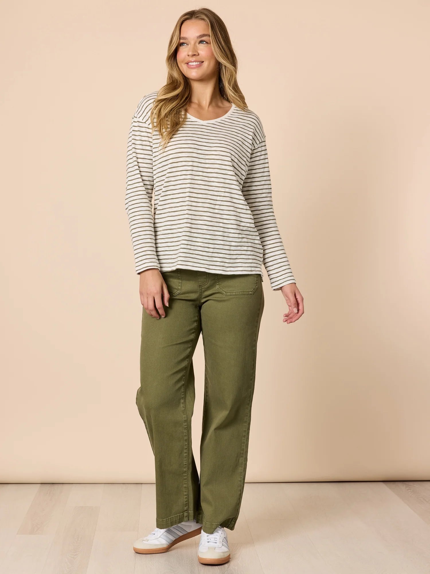 Woman wearing a Threadz striped long-sleeve top and green pants against a beige background