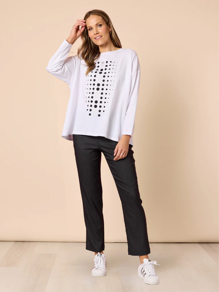 Image of Woman wearing a white top with black polka dots and Threadz black pants against a beige background