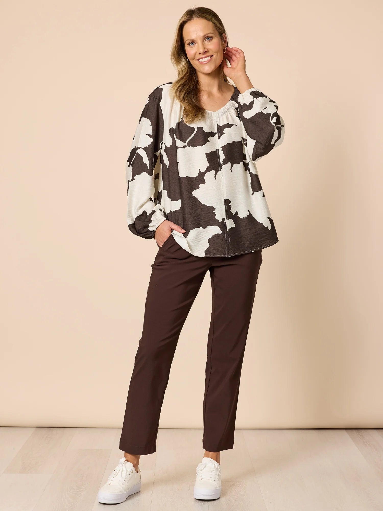 Woman wearing a floral sweater and Threadz brown pants on a beige background