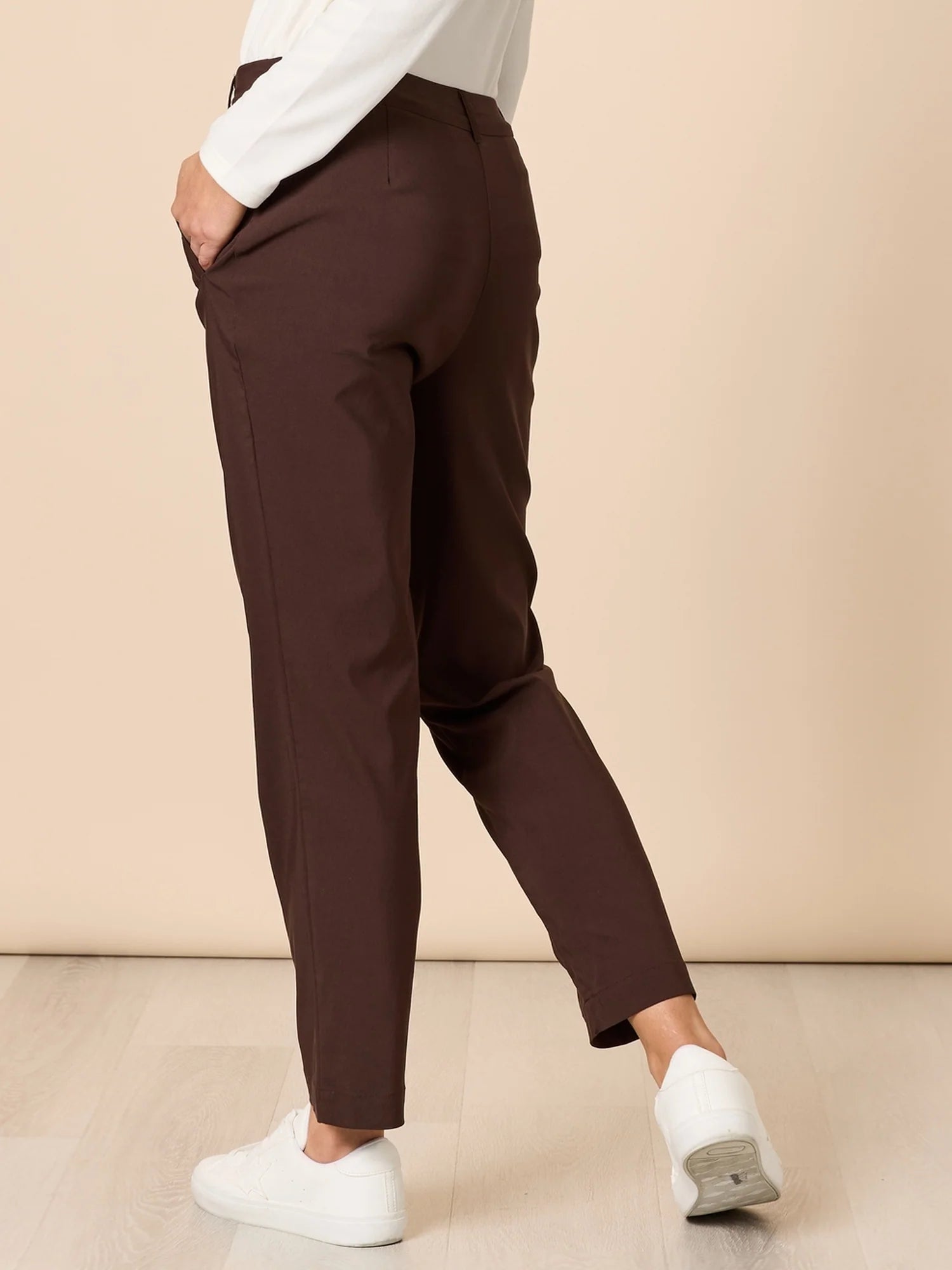 Image of Woman wearing Threadz brown pants and white shoes on a beige background