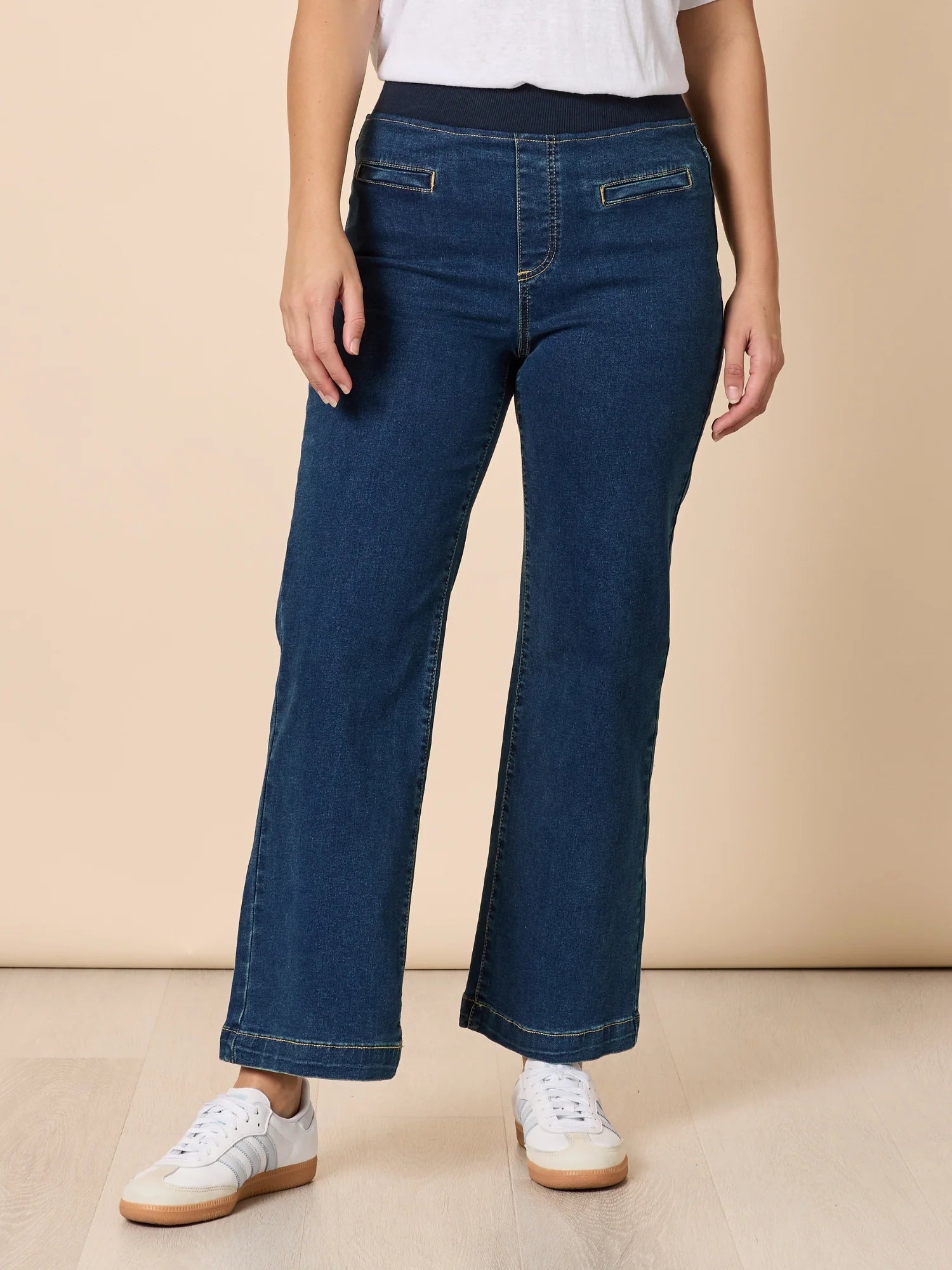 Image of Woman wearing Threadz blue jeans and white sneakers on a beige background