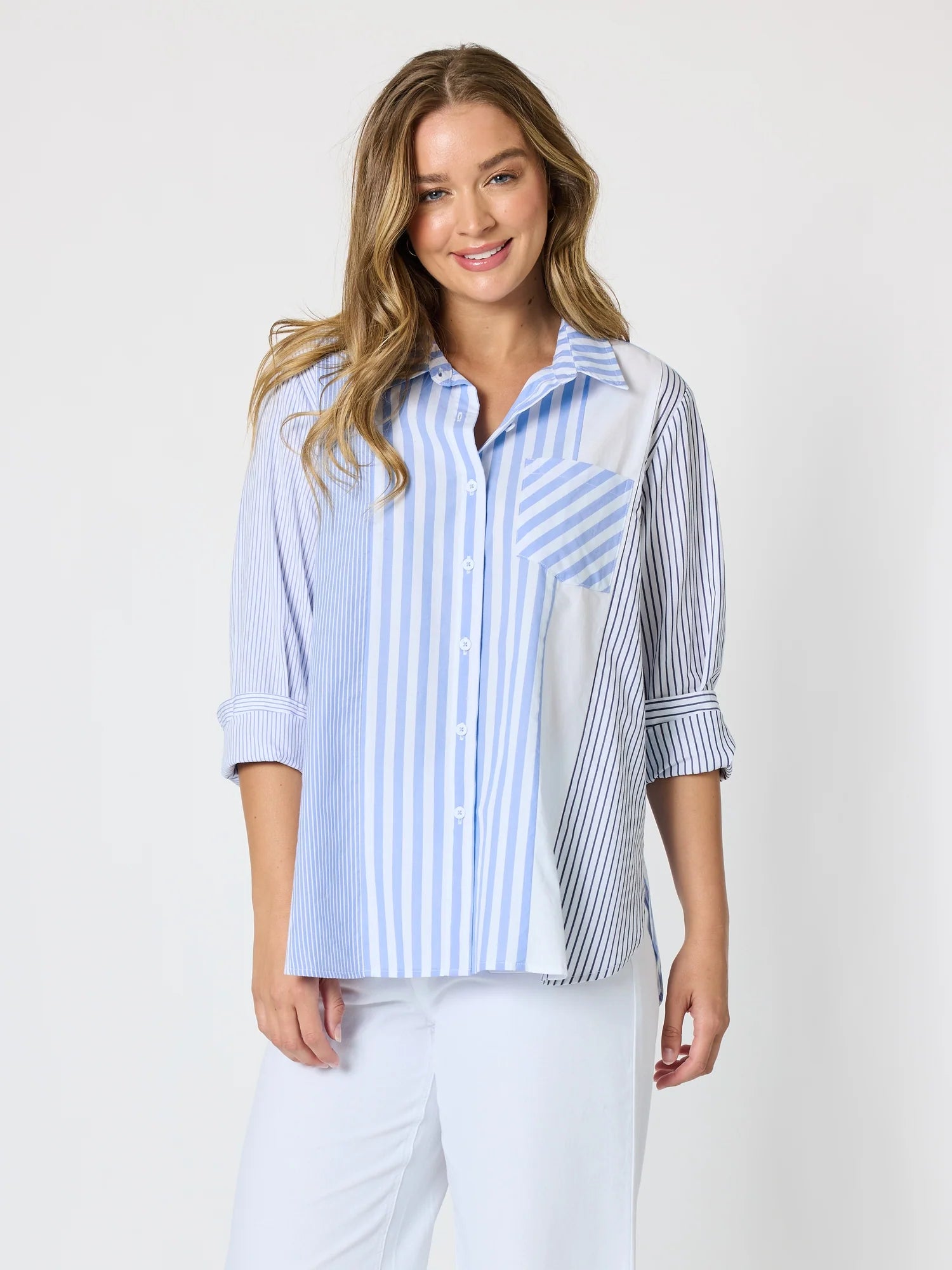 Image of Woman pictured on a plain background wearing a blue & white Threadz stripe button up paired with white jeans 