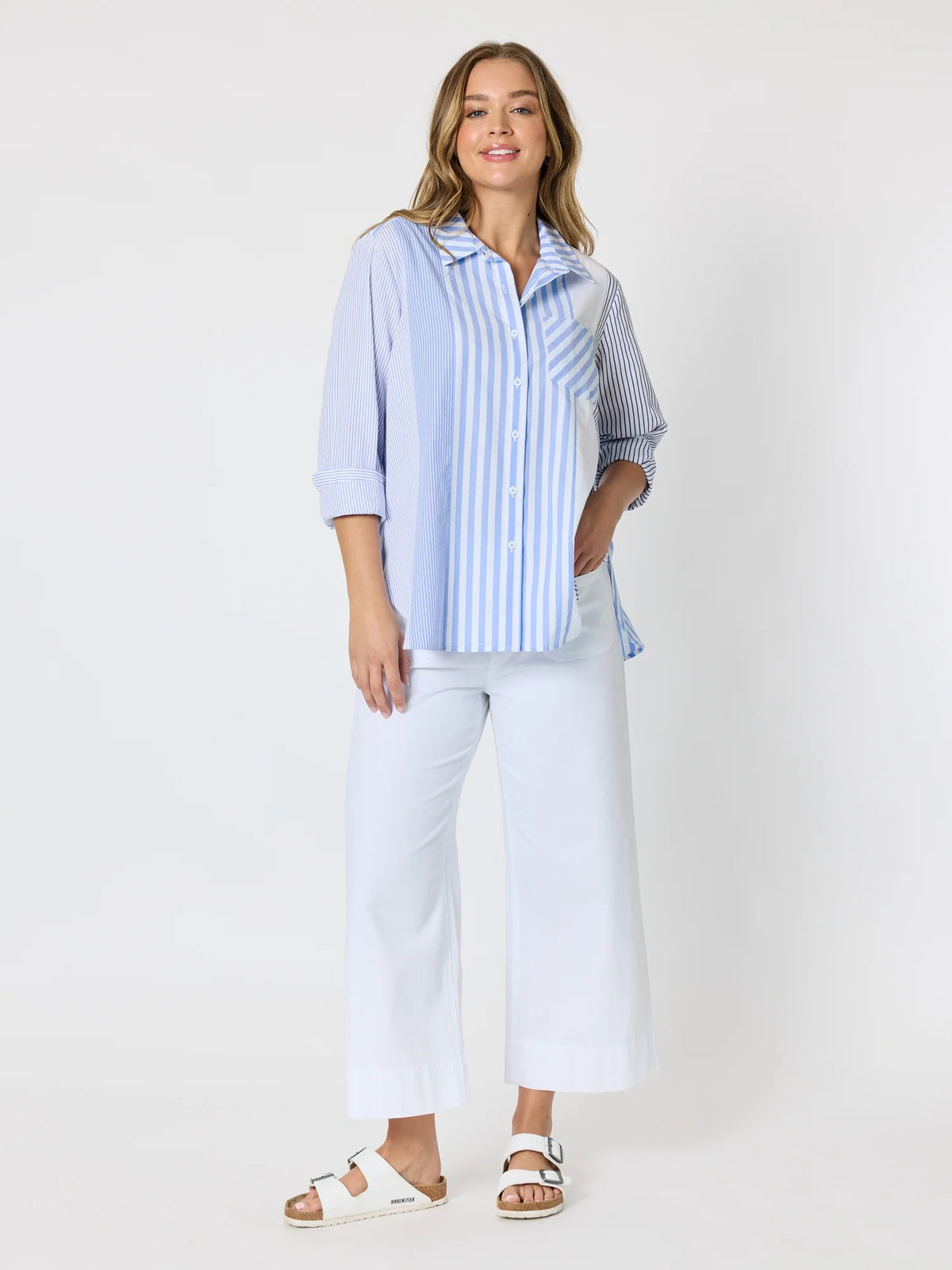 Woman pictured on a plain background wearing a blue & white Threadz stripe button up paired with white jeans 