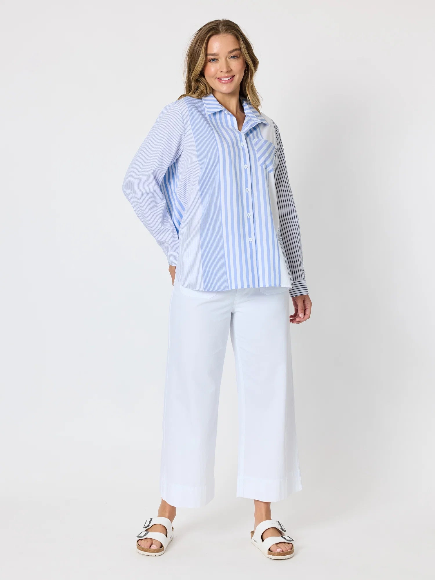 Image of Woman pictured on a plain background wearing a blue & white Threadz stripe button up paired with white jeans 