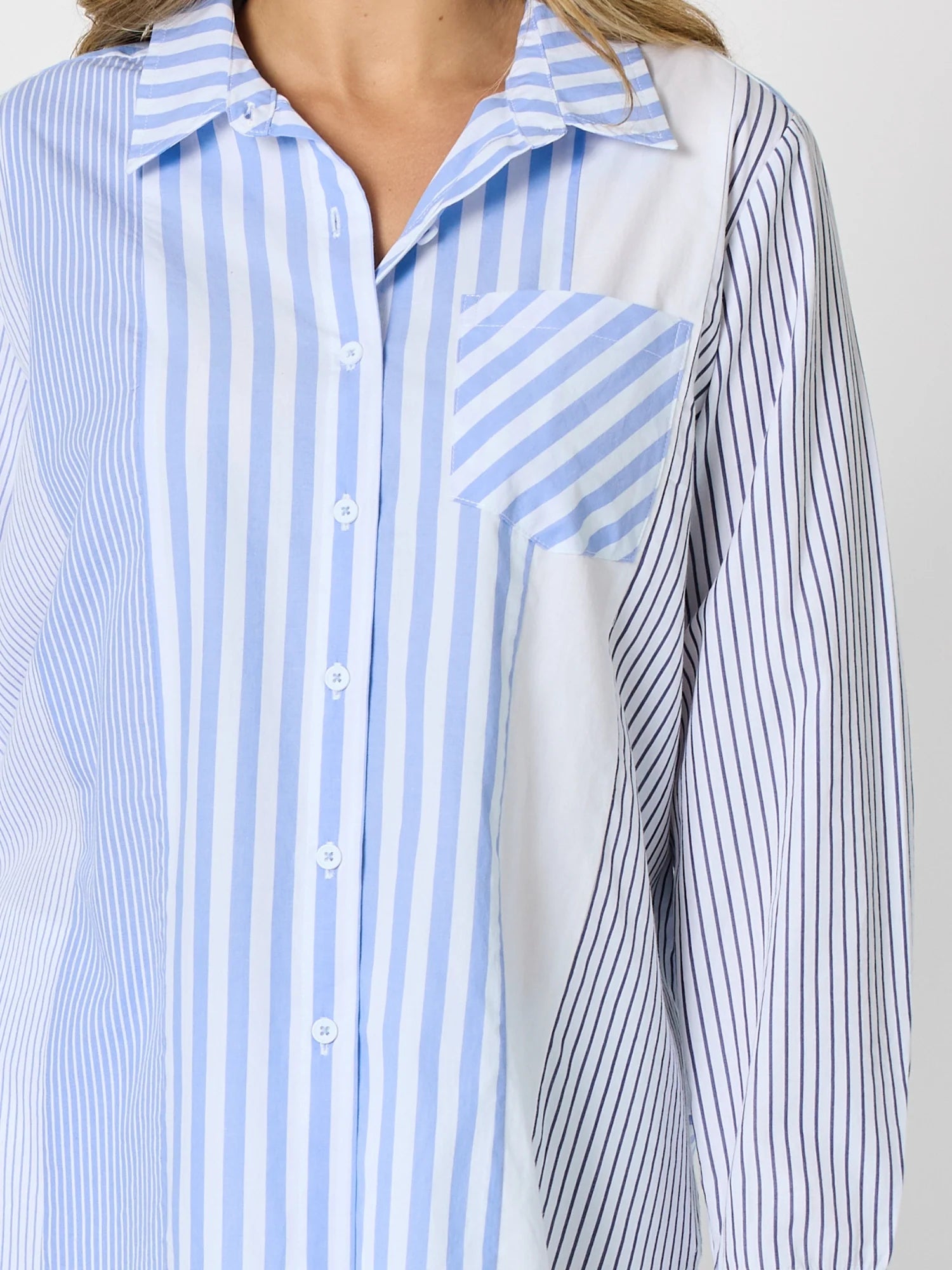 Image of Woman pictured on a plain background wearing a blue & white Threadz stripe button up paired with white jeans 