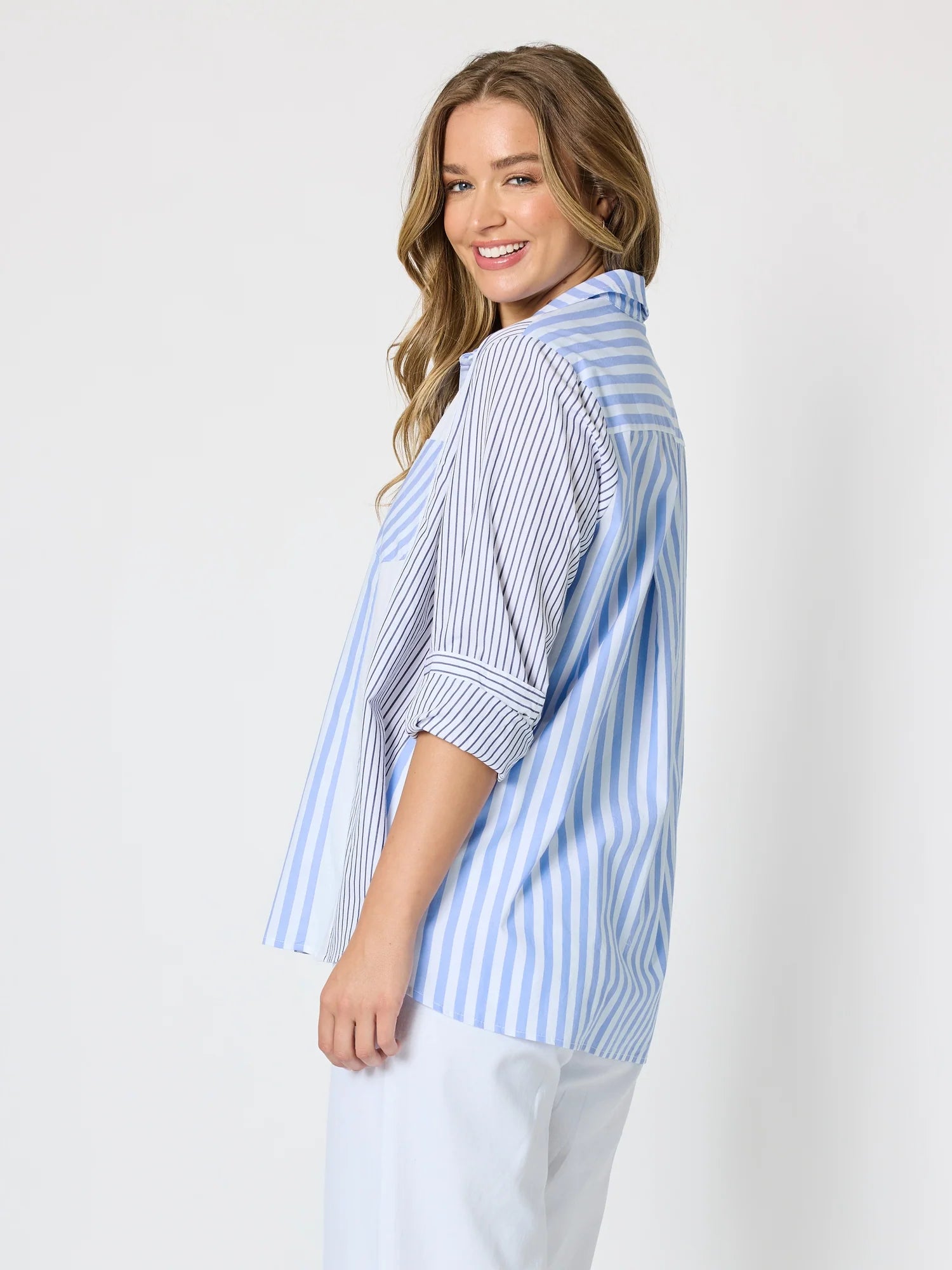 Image of Woman pictured on a plain background wearing a blue & white Threadz stripe button up paired with white jeans 