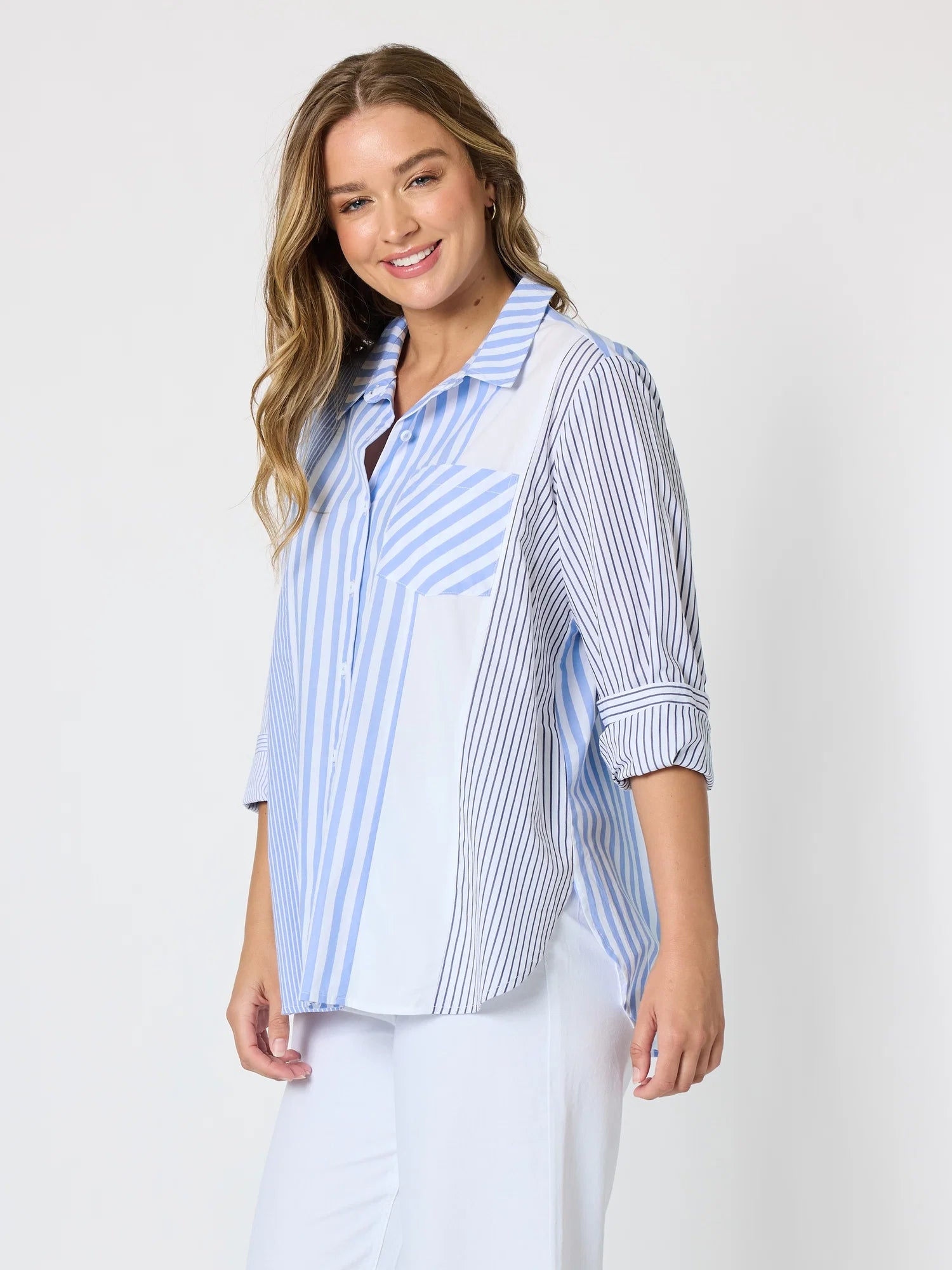 Image of Woman pictured on a plain background wearing a blue & white Threadz stripe button up paired with white jeans 