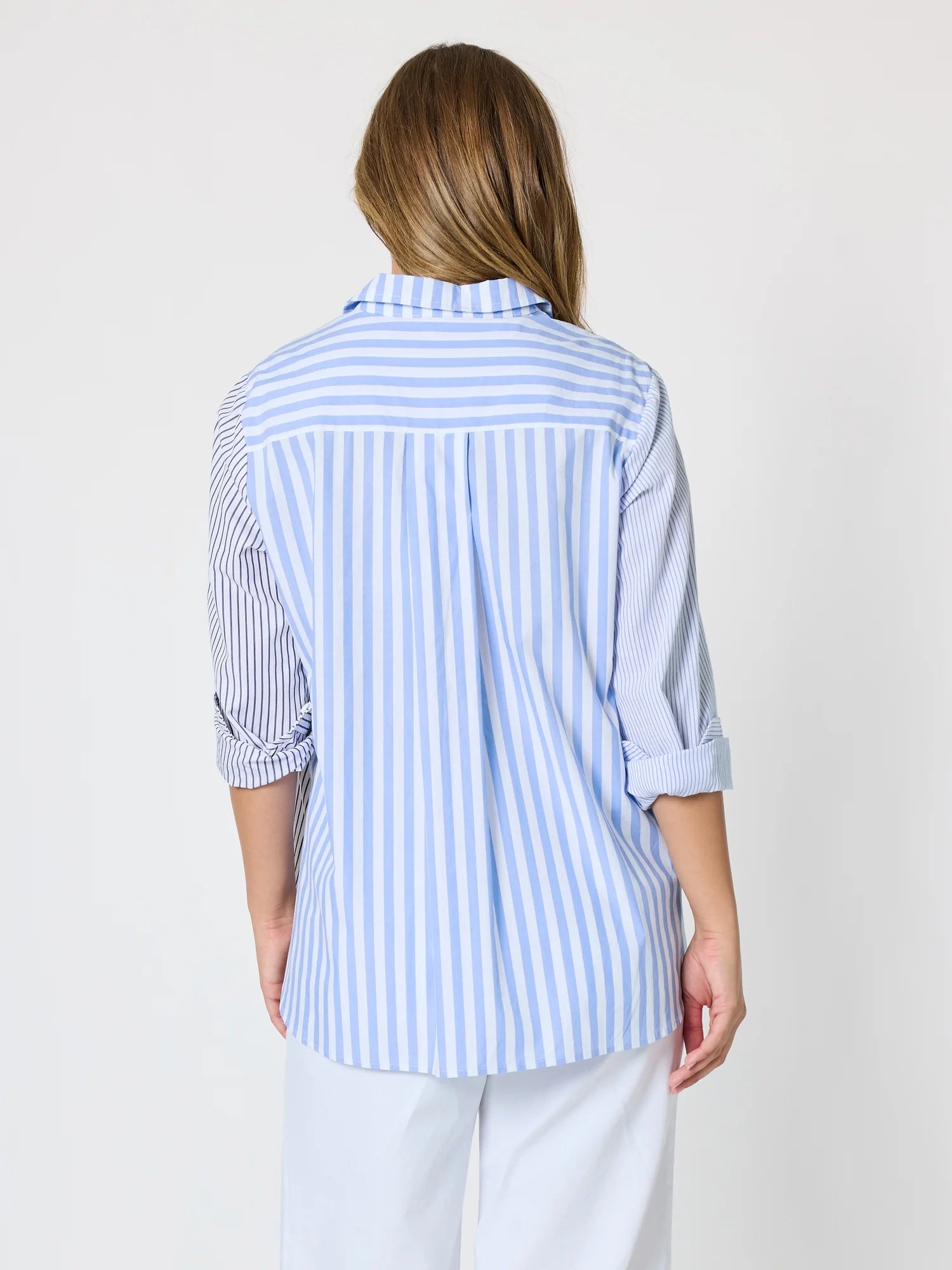 Image of Woman pictured on a plain background wearing a blue & white Threadz stripe button up paired with white jeans 