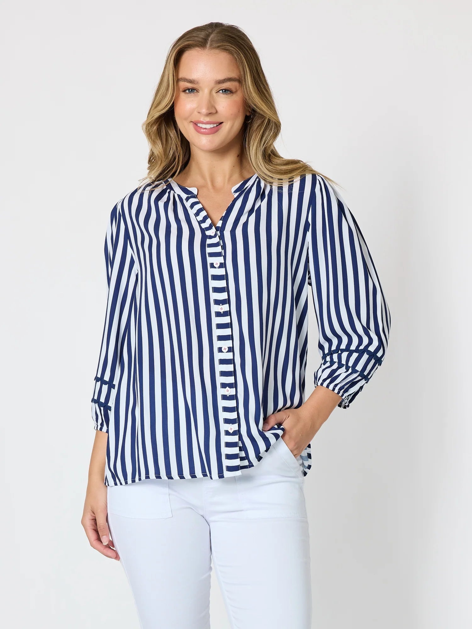 Image of A woman modeling a Threadz navy and white vertically striped button-down blouse with three-quarter sleeves, paired with white pants, against a light gray studio background.