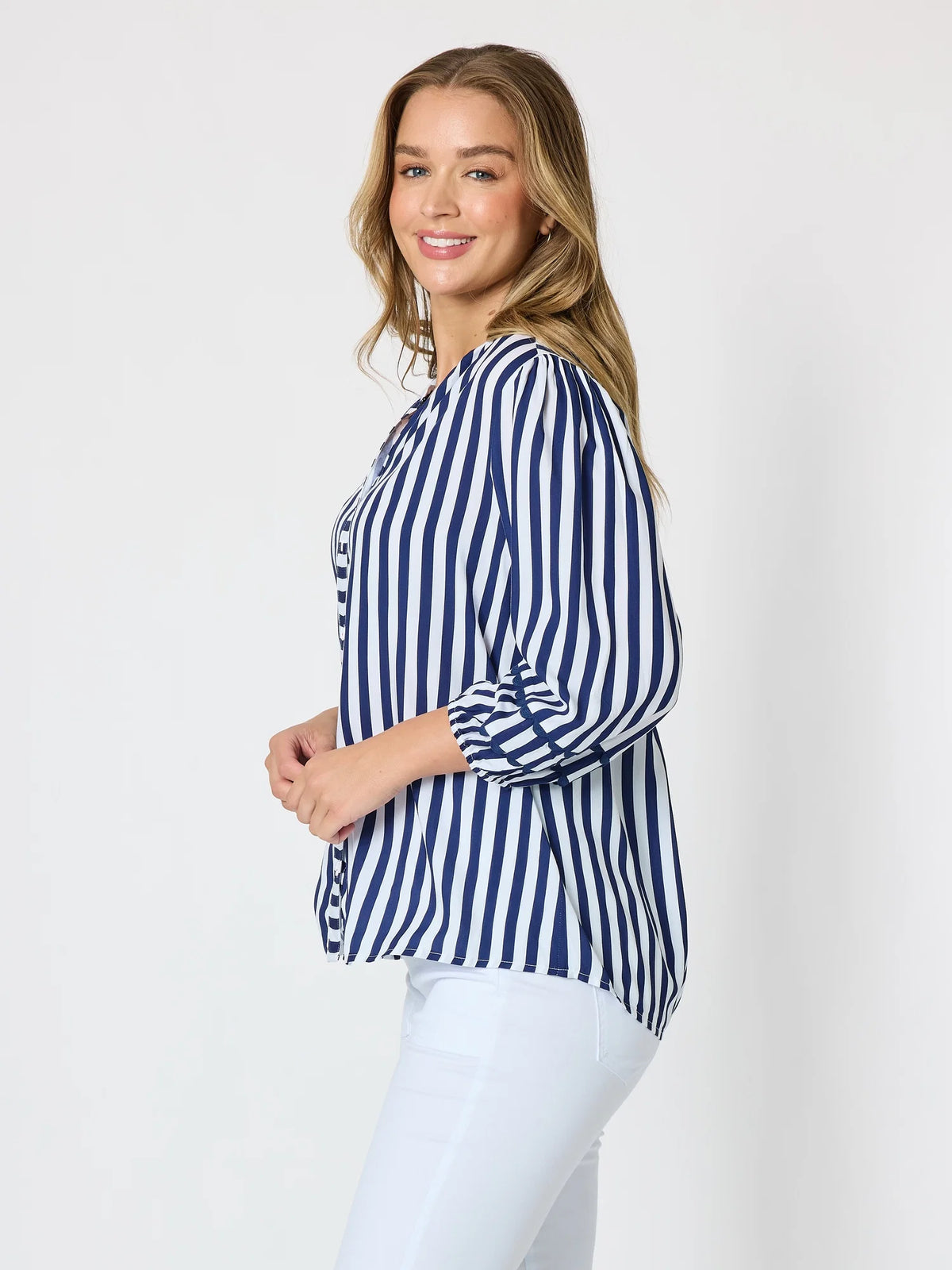 A woman modeling a Threadz navy and white vertically striped button-up blouse with three-quarter sleeves, paired with white pants, against a plain light gray studio background.