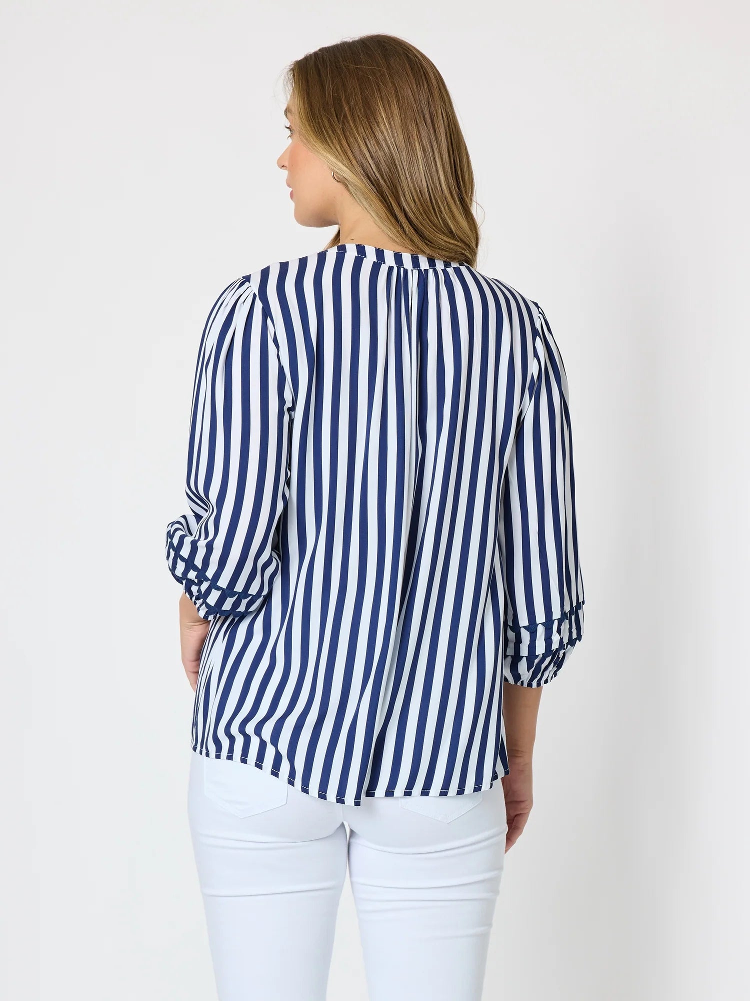 Image of A woman shown from the back wearing a Threadz navy and white vertically striped blouse with three-quarter sleeves and white pants, against a plain light gray studio background.