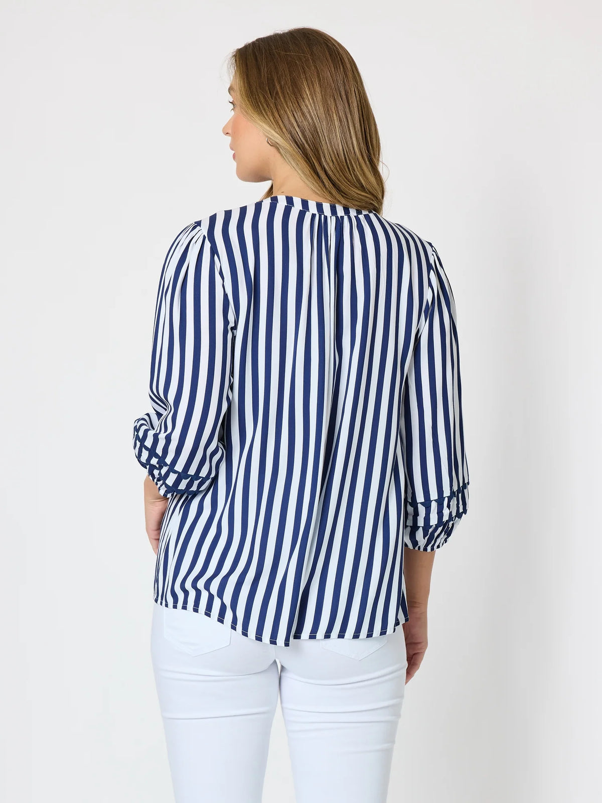 A woman shown from the back wearing a Threadz navy and white vertically striped blouse with three-quarter sleeves and white pants, against a plain light gray studio background.