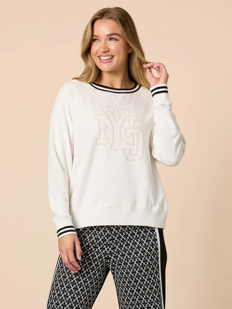 Woman wearing a Threadz white sweater with black trim and patterned pants on a beige background