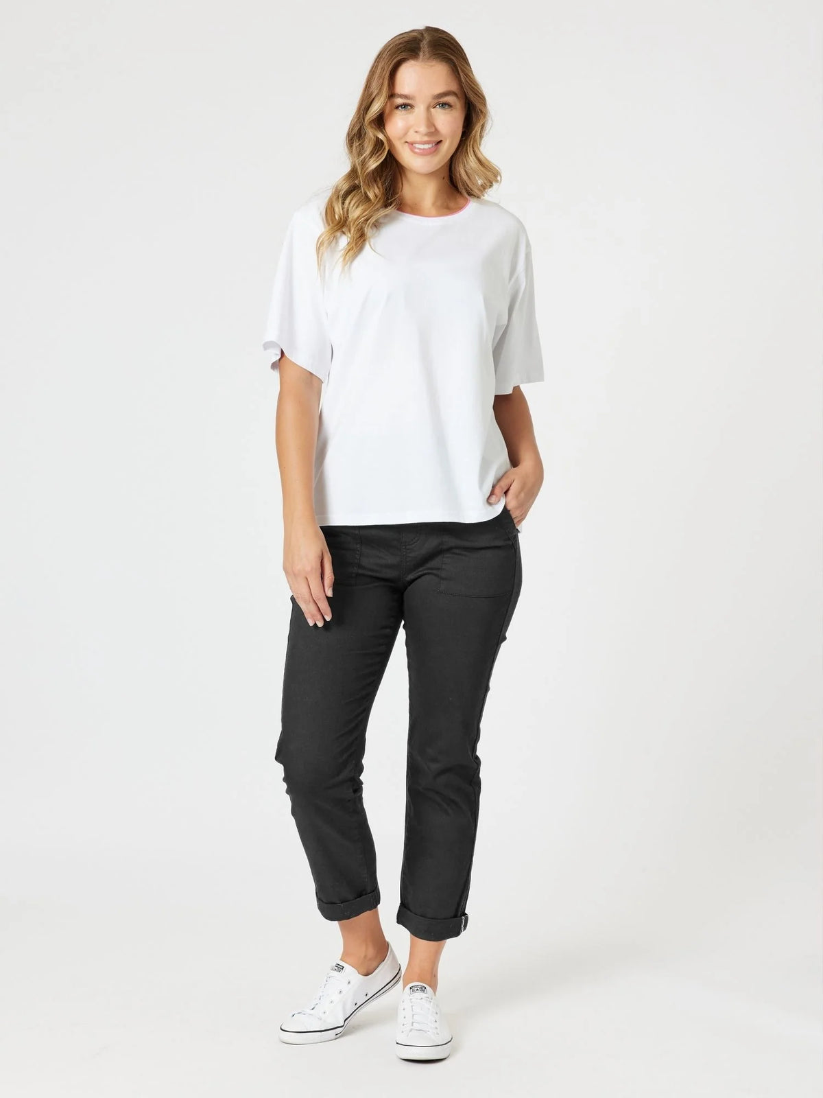 A woman modeling a white short-sleeve crewneck t-shirt and Threadz black cropped pants with white sneakers, standing against a plain white studio background.