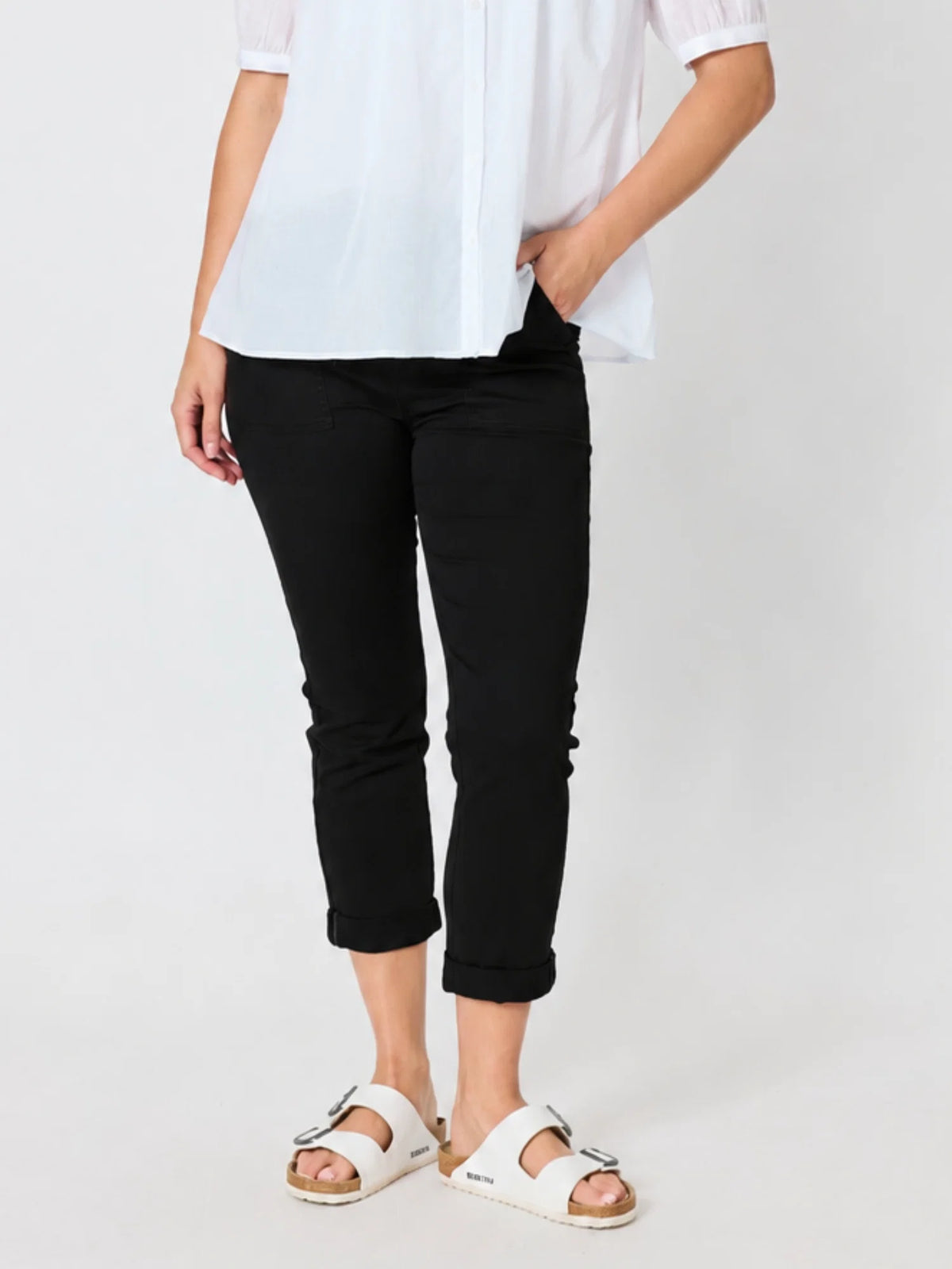 A model wearing Threadz black cropped pants, a white blouse, and white slide sandals, standing against a plain light gray studio background.