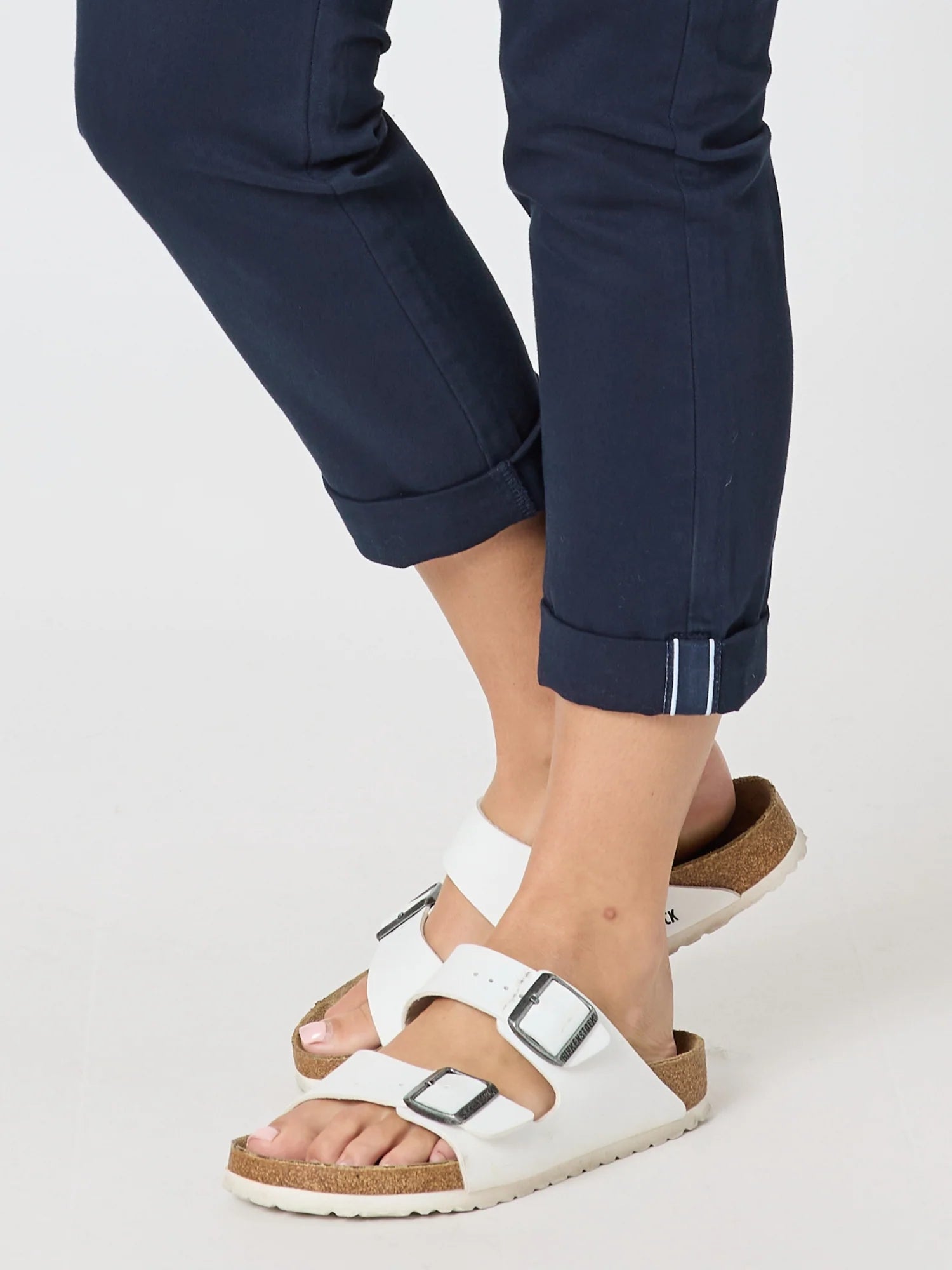 Image of White double-strap slide sandals with adjustable buckles and a cork-look midsole, shown worn with Threadz  navy cuffed pants on a light gray studio background.