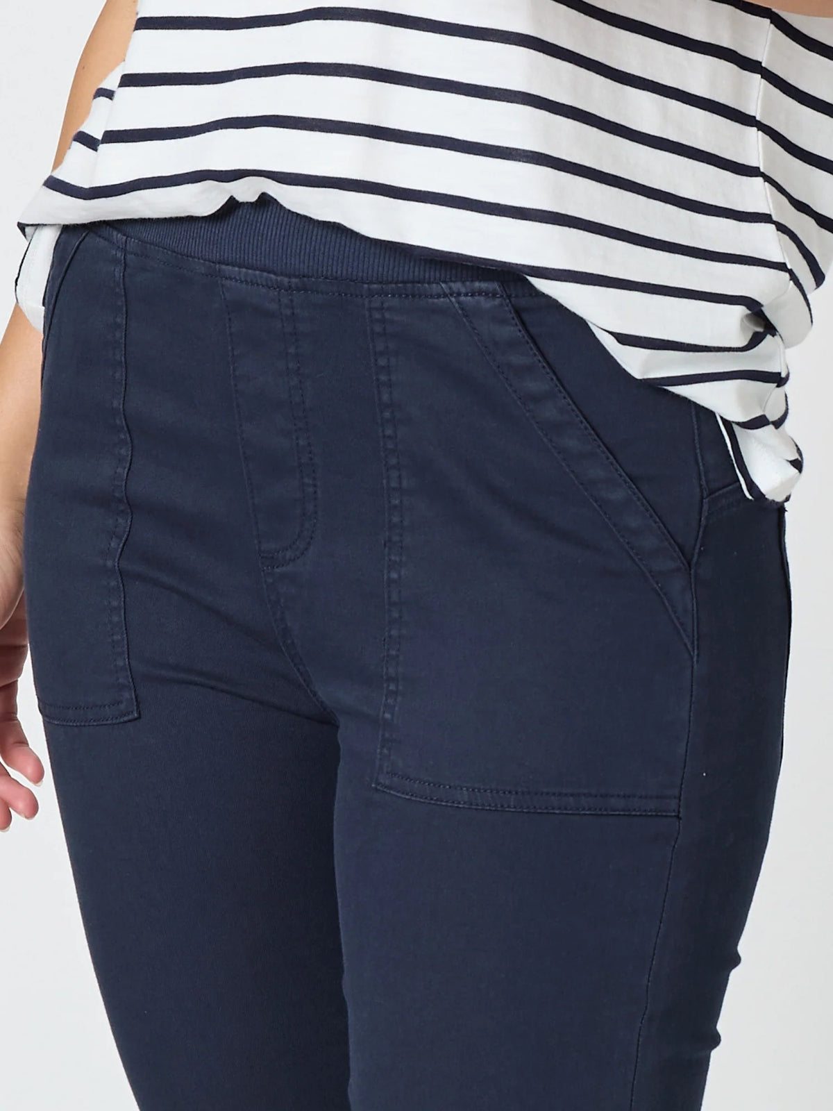 Close-up of a woman wearing Threadz navy blue pants and a white top with navy horizontal stripes, cropped from the chest down against a light gray background.