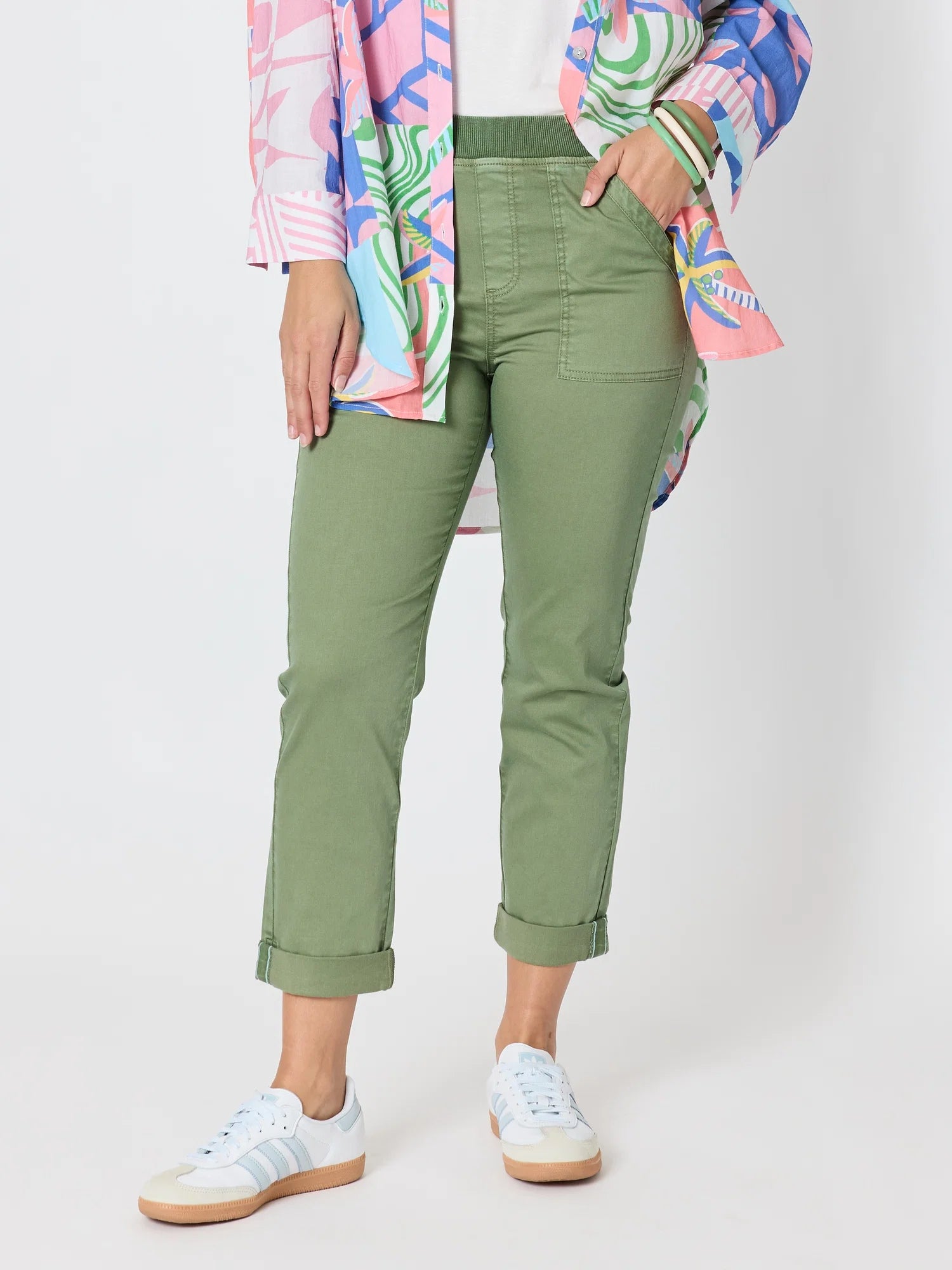 Image of A model wearing Threadz olive green cropped pants with rolled cuffs, styled with a colorful patterned shirt and white sneakers against a light gray studio background.