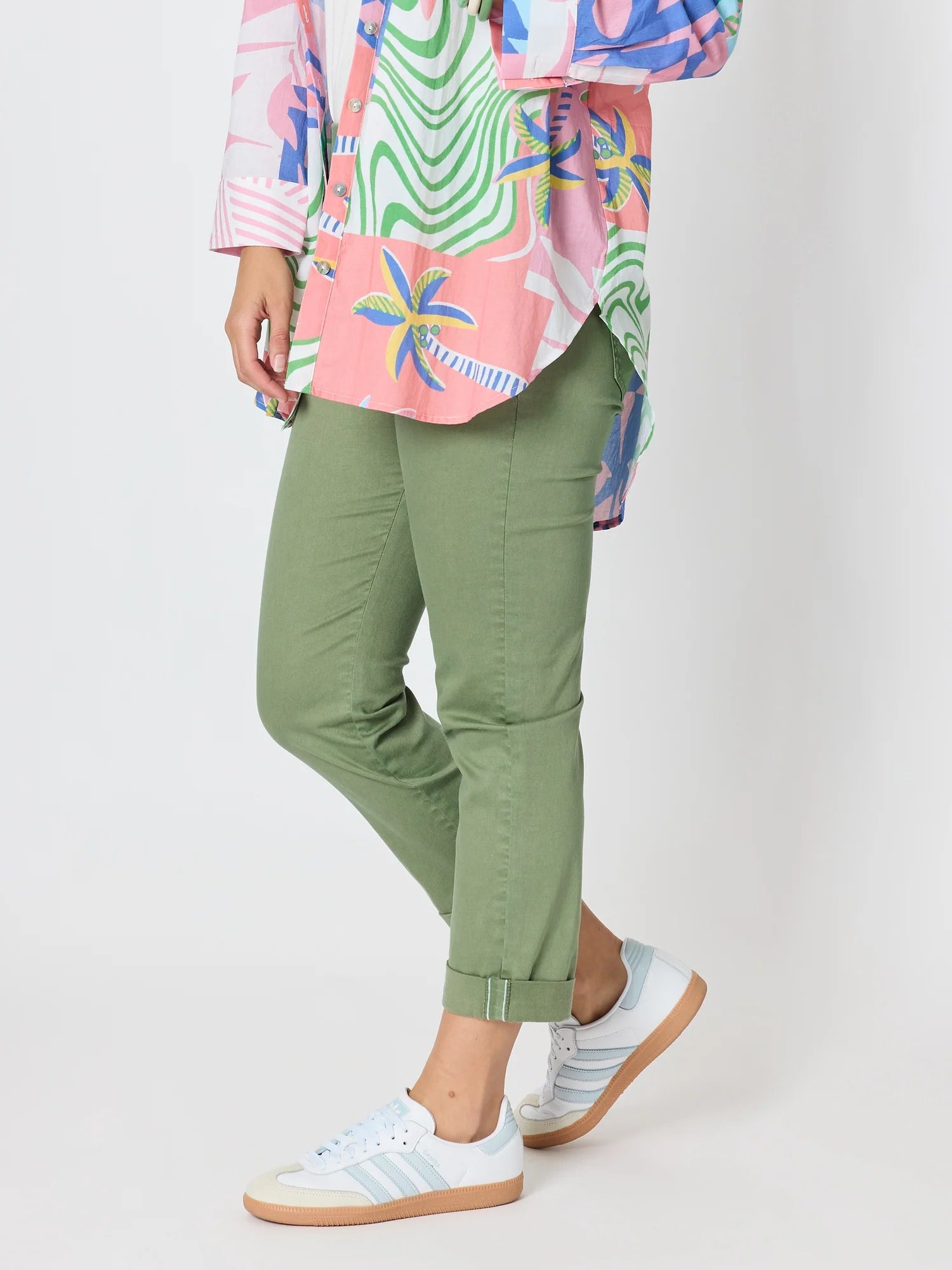 Image of A woman wearing Threadz olive green cropped pants with a colorful tropical print shirt and white sneakers, shown from the waist down against a light gray studio background.