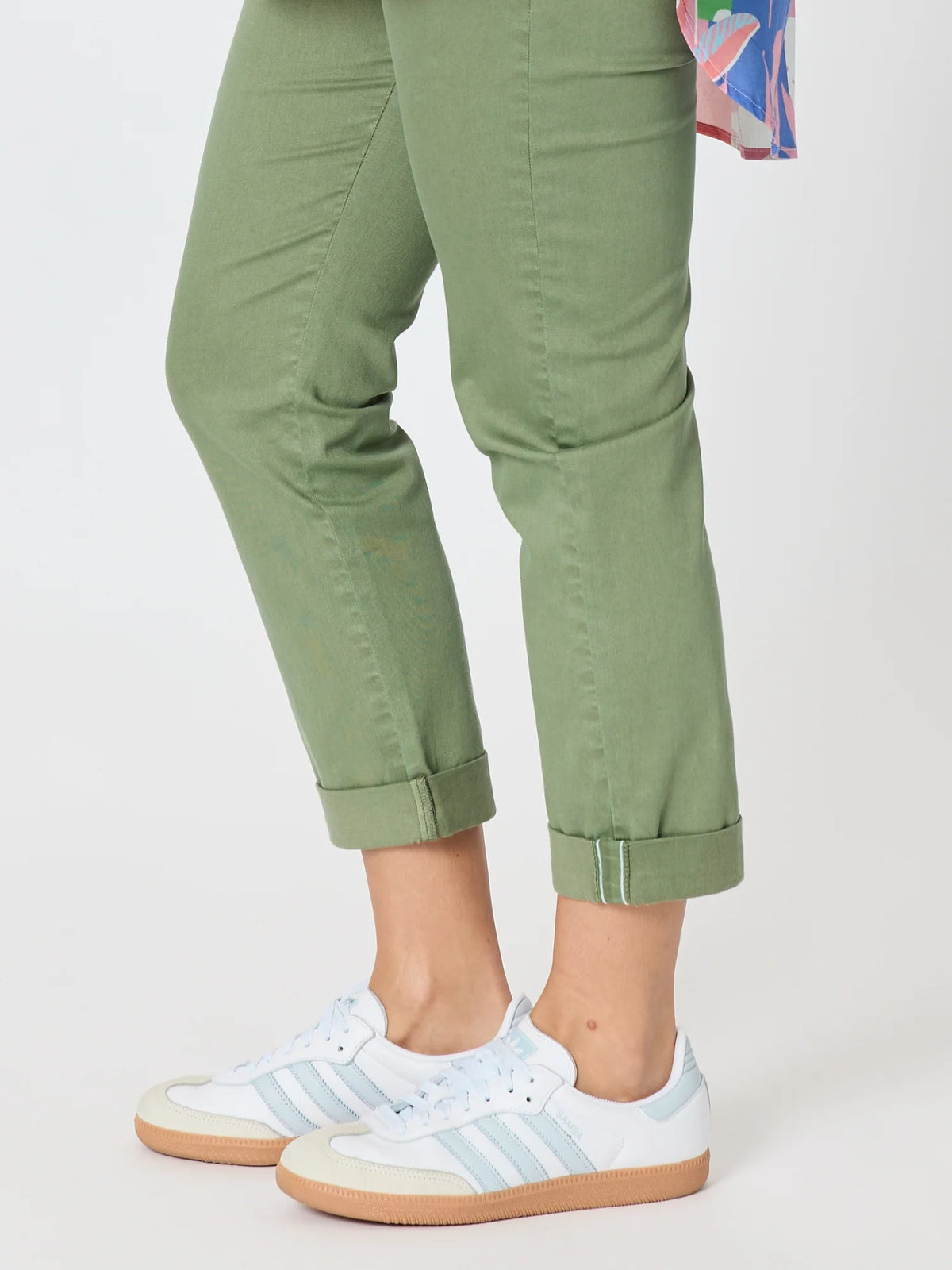A woman wearing Threadz sage green cropped pants with rolled cuffs and white low-top sneakers with light blue stripes, shown from the waist down on a light gray studio background.