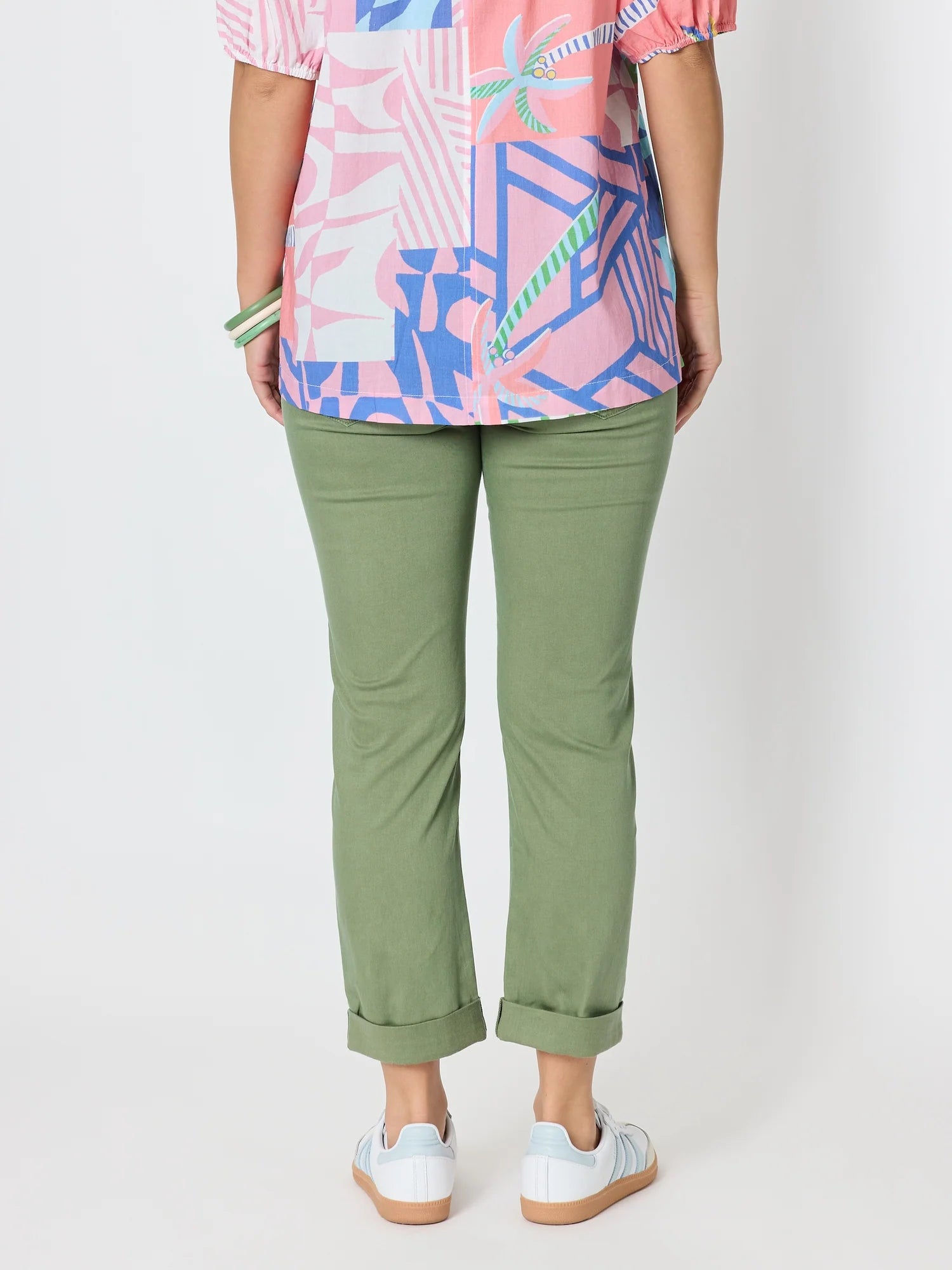 Image of A woman shown from the back wearing Threadz olive green cropped pants with rolled cuffs, a colorful patterned top, and white sneakers against a plain light gray studio background.