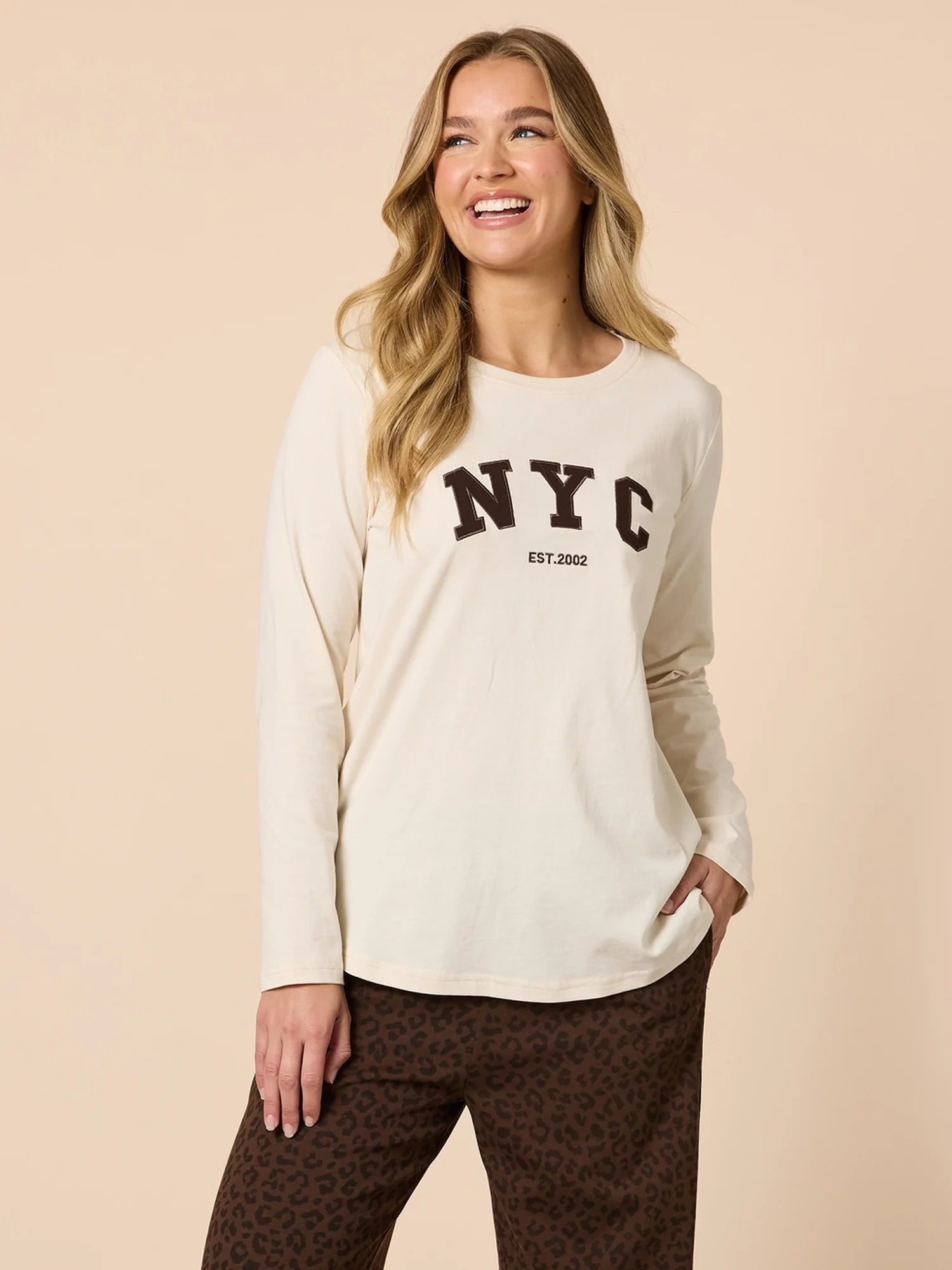 Woman wearing a Threadz cream long-sleeve shirt with 'NYC' print on a beige background