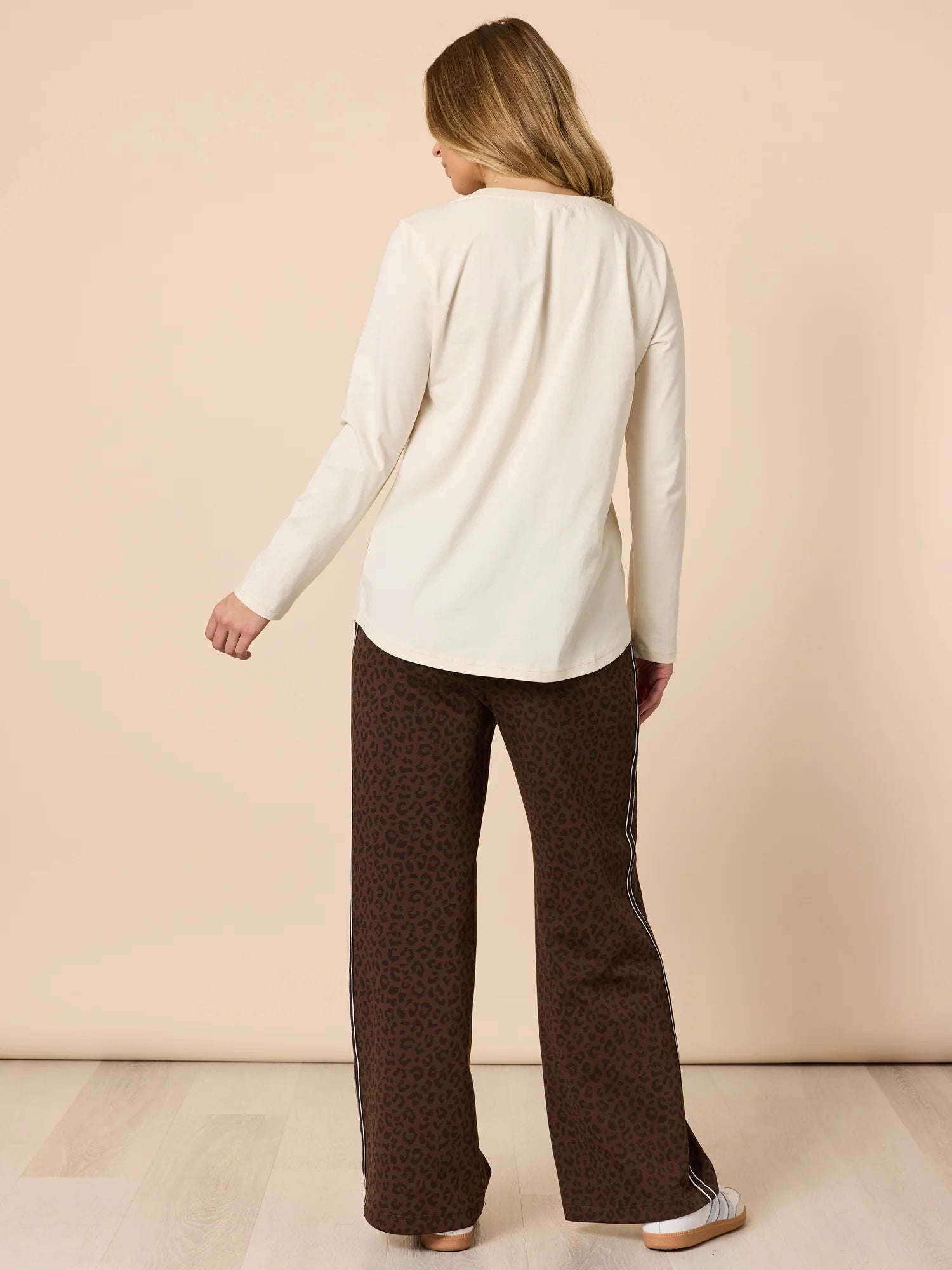 Woman wearing a Threadz white sweater and brown patterned pants on a beige background