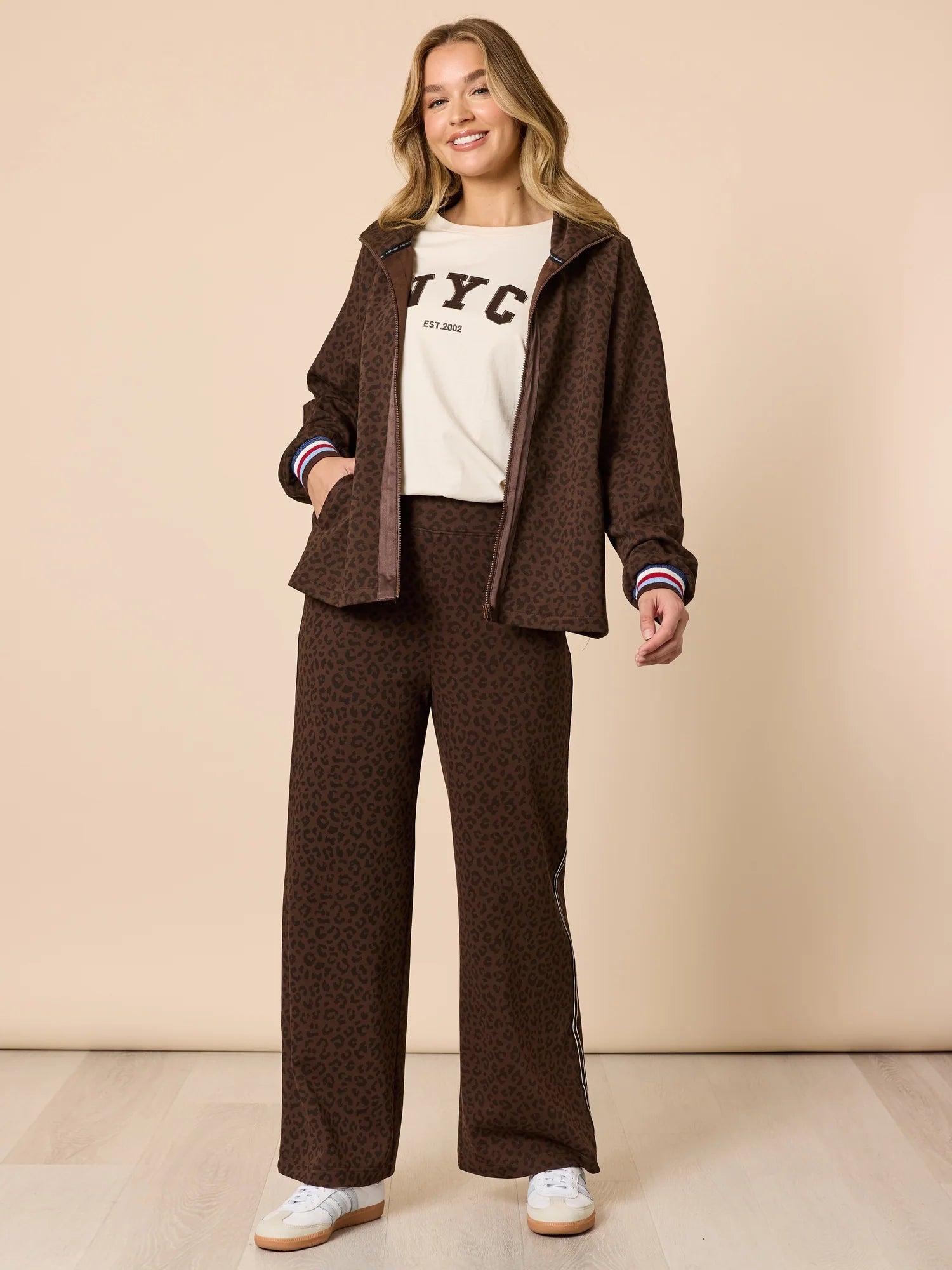 Woman wearing a brown jacket and pants with a Threadz white shirt featuring 'NYC' text on a beige background