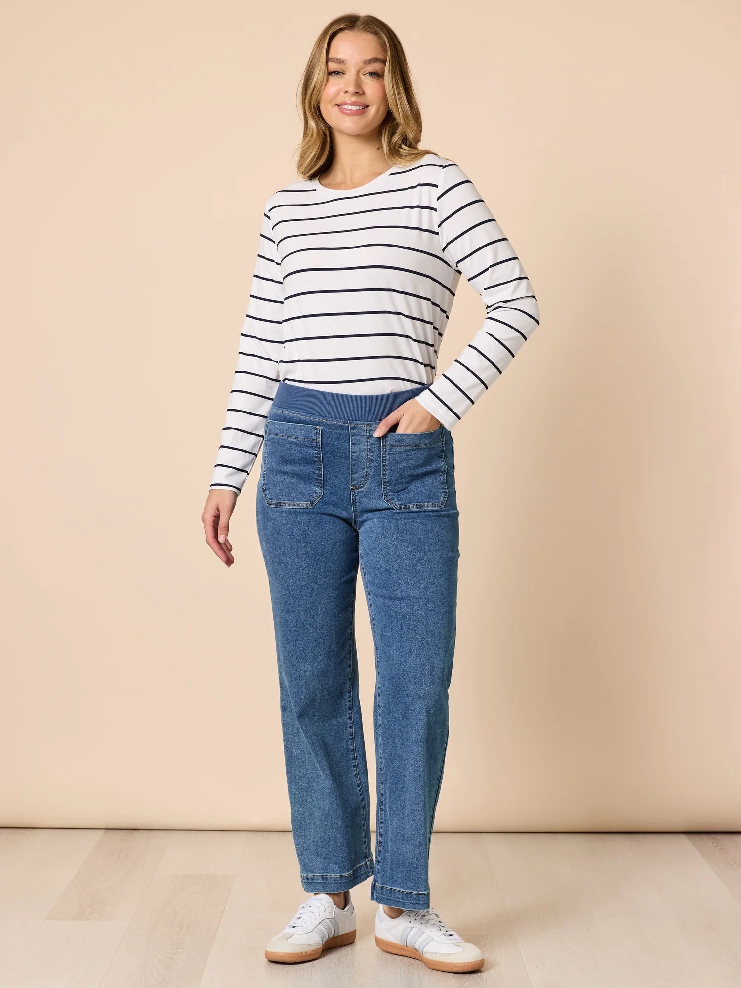 Image of Woman wearing a Threadz striped long-sleeve top and blue jeans on a beige background