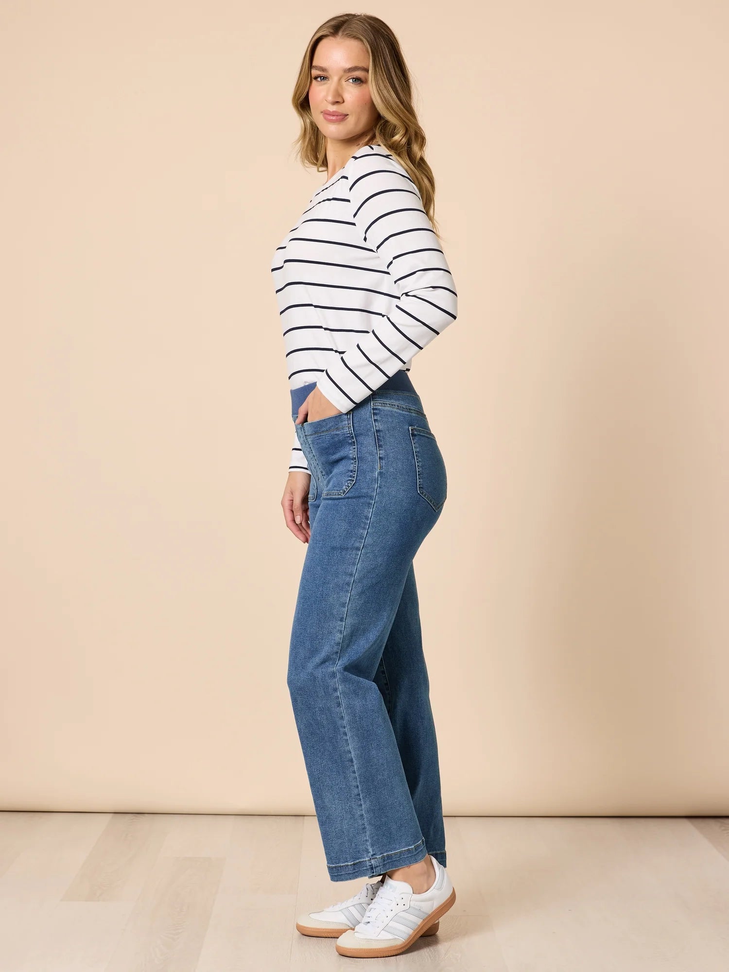 Image of Woman wearing a Threadz striped sweater and blue jeans against a beige background
