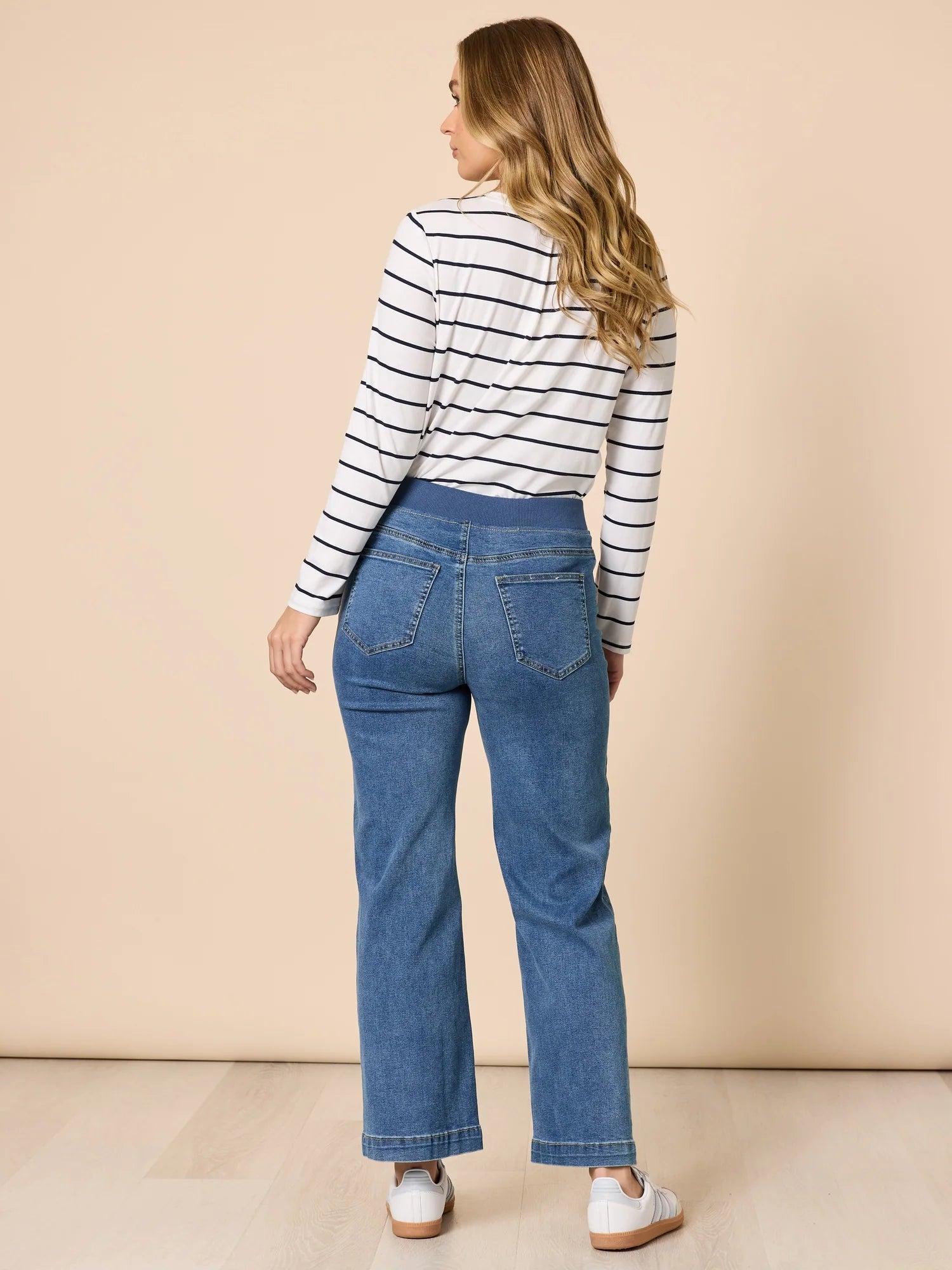 Image of Woman wearing a Threadz striped shirt and blue jeans against a beige background