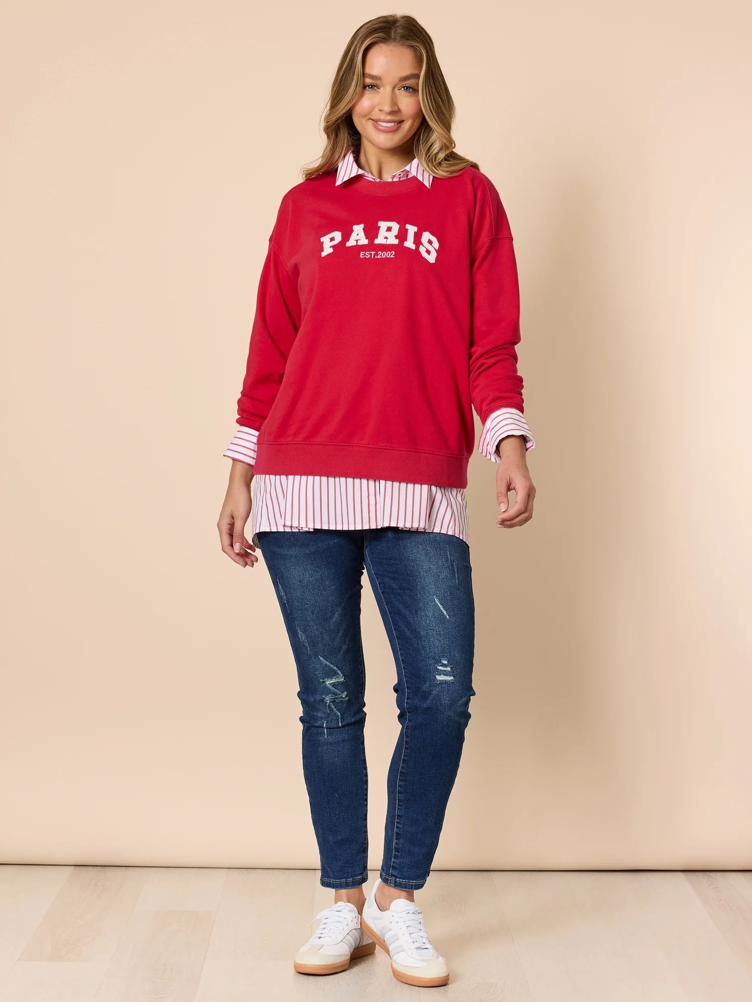 Woman wearing a Threadz red 'PARIS' sweatshirt and blue jeans on a beige background