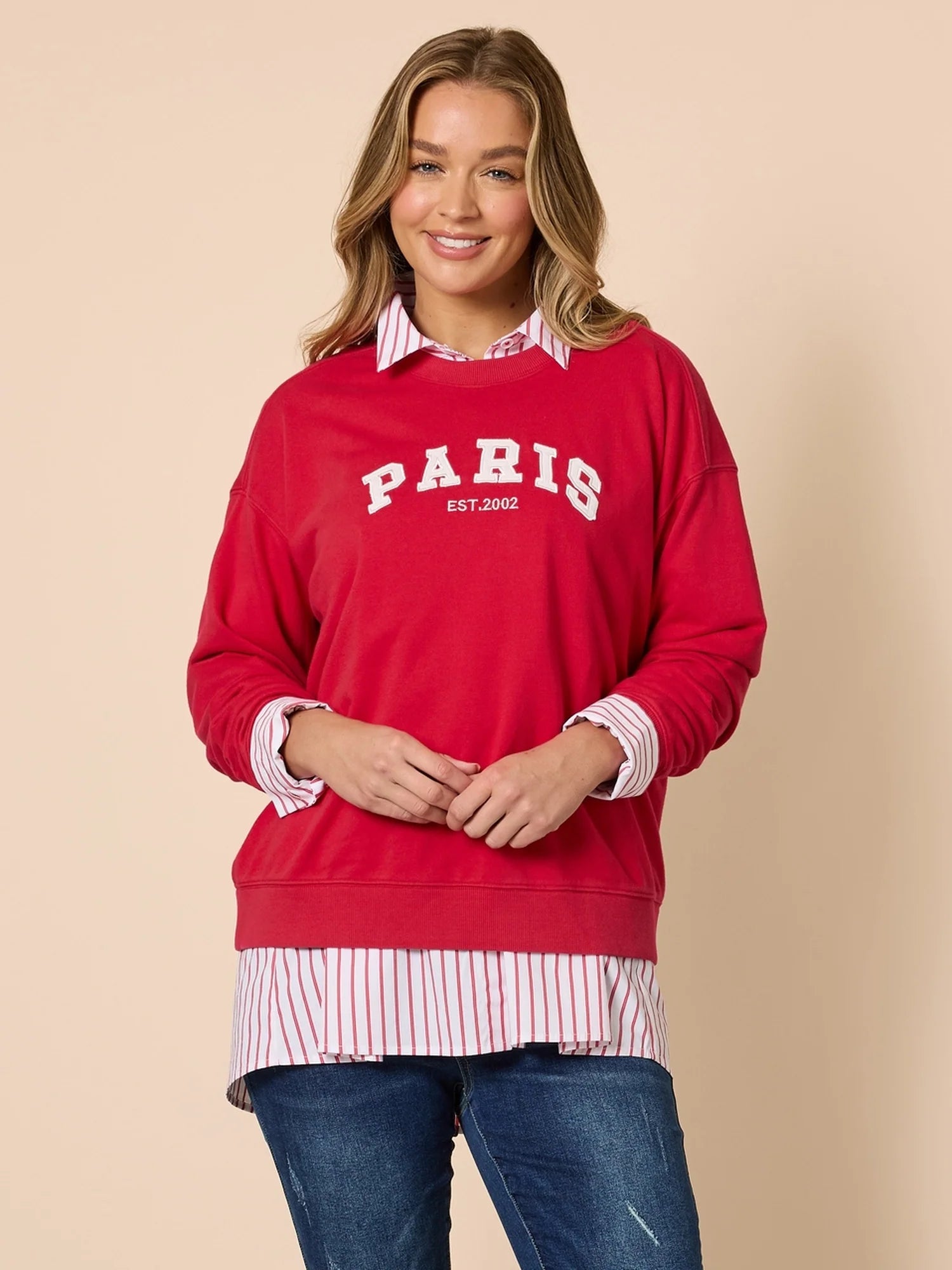 Woman wearing a Threadz red 'PARIS' sweatshirt over a striped shirt with a beige background