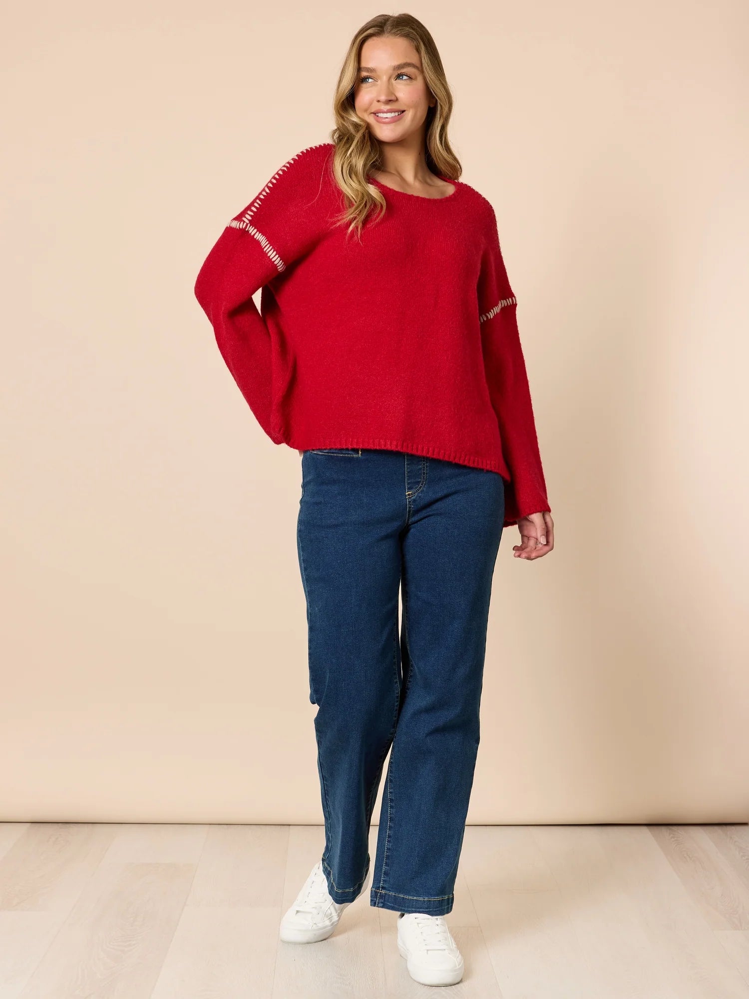 Woman wearing a Threadz red sweater and blue jeans against a beige background