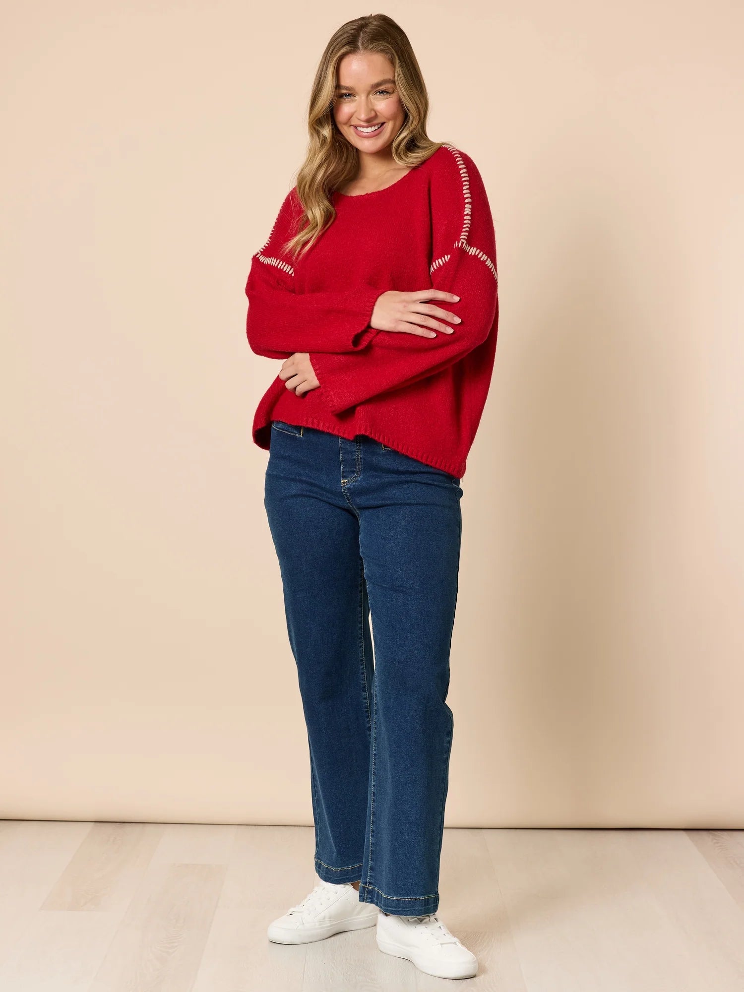 Woman wearing a Threadz red sweater and blue jeans against a beige background
