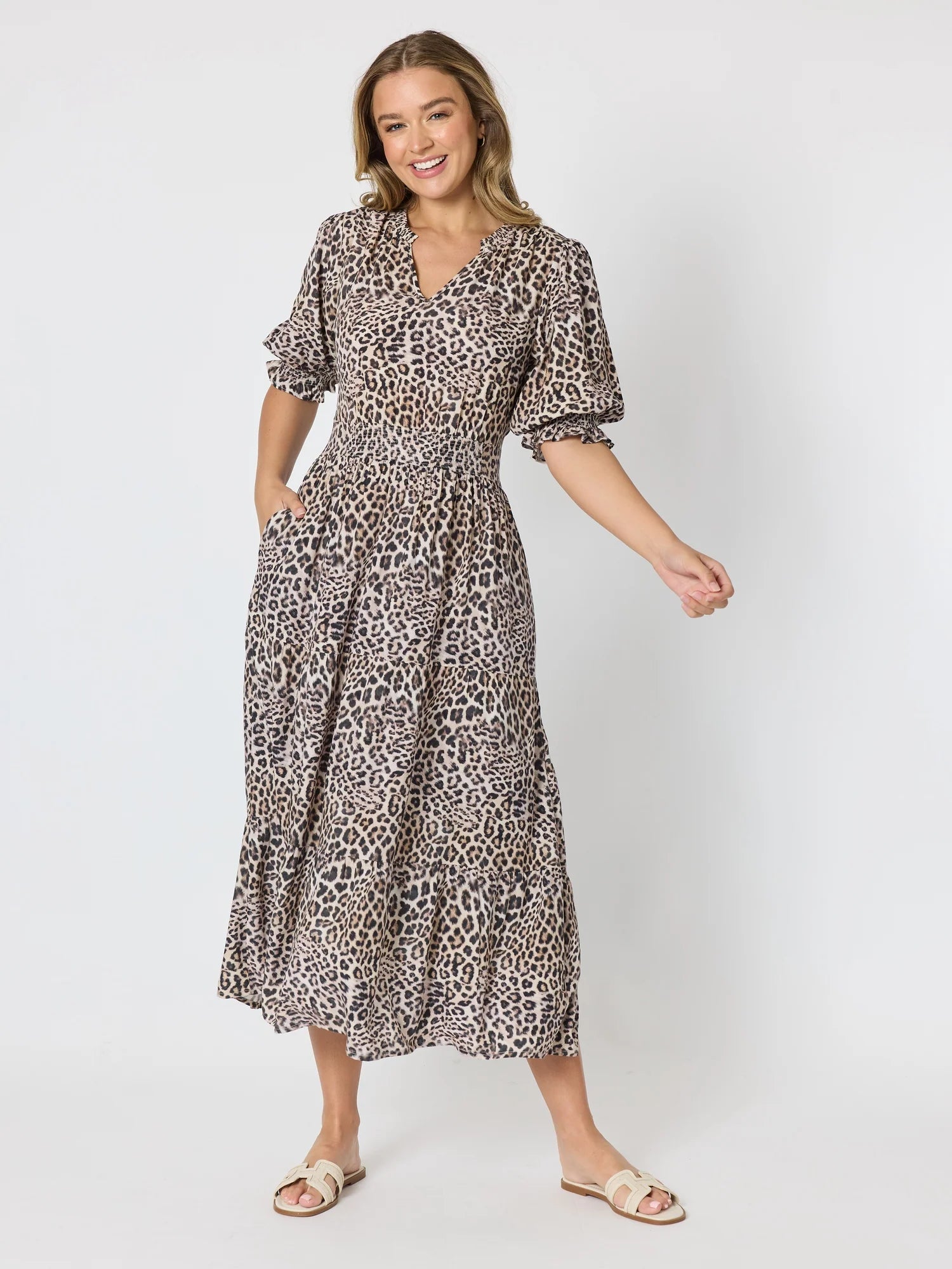 Image of A woman modeling a Threadz leopard-print midi dress with puff sleeves and a V-neckline, paired with beige slide sandals, against a light gray studio background.