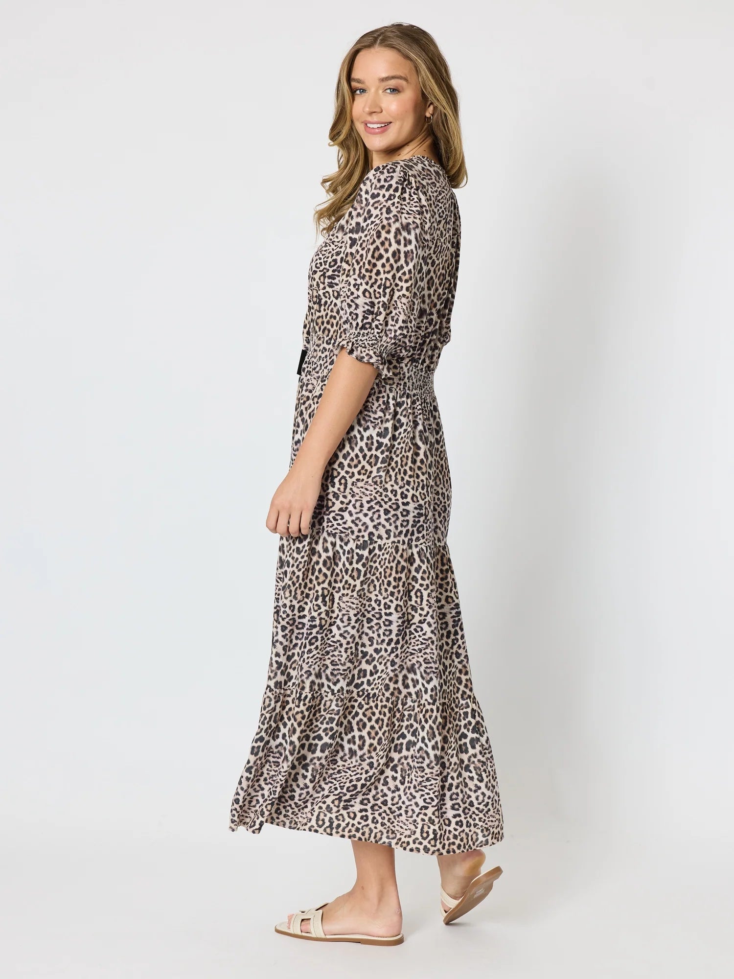 A woman modeling a Threadz leopard-print midi dress with three-quarter sleeves and a matching fabric belt, shown from a side-back angle against a light gray studio background.