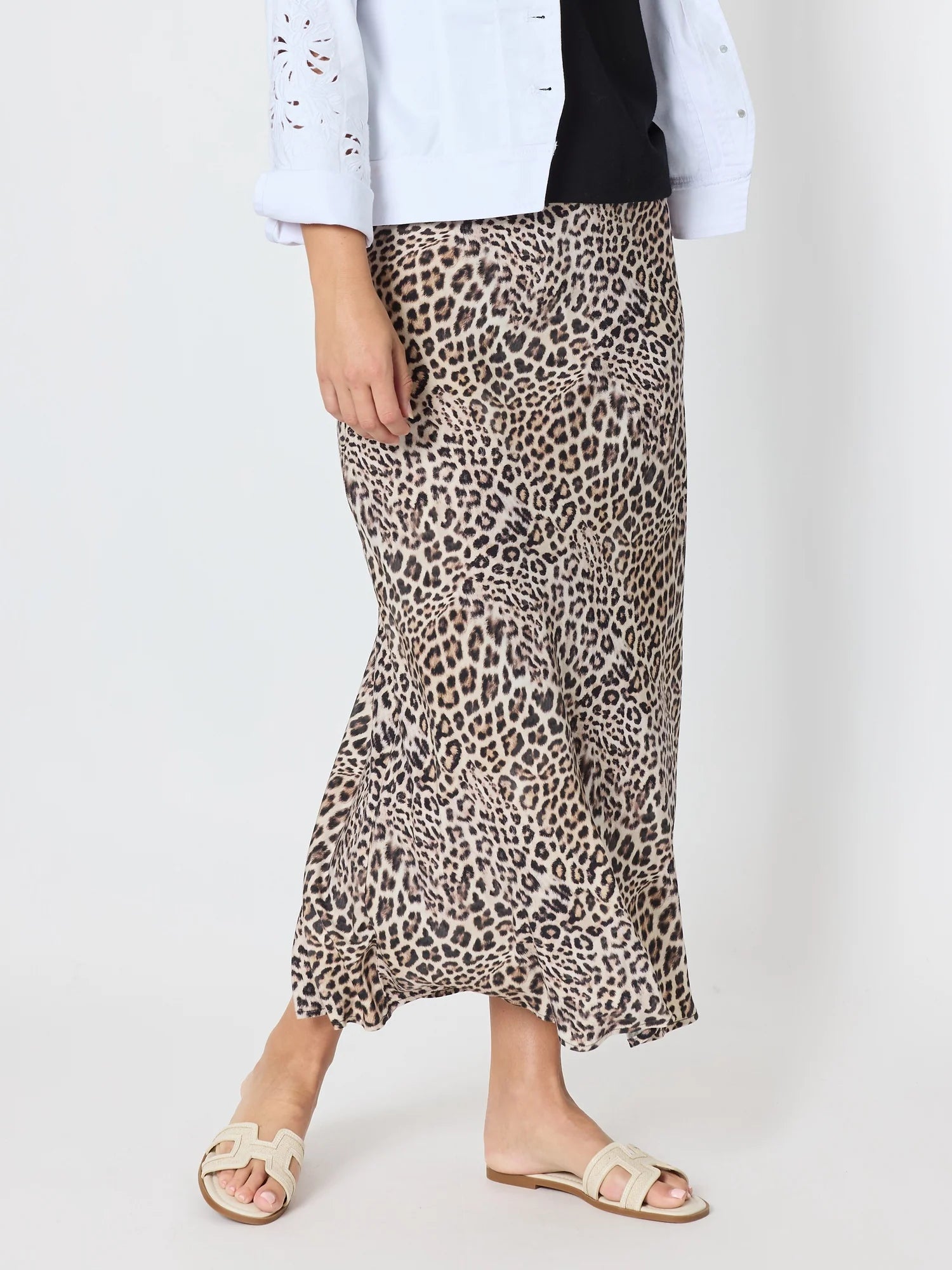Image of A woman wearing a Threadz leopard print midi skirt with a flared hem, styled with a white cropped jacket, black top, and beige slide sandals against a plain light background.