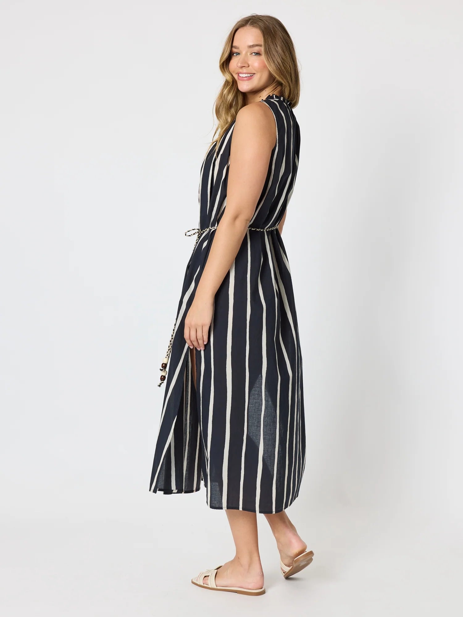 Image of A woman modeling a Threadz sleeveless midi dress with vertical navy and white stripes, shown from a side-back angle against a light gray studio background.
