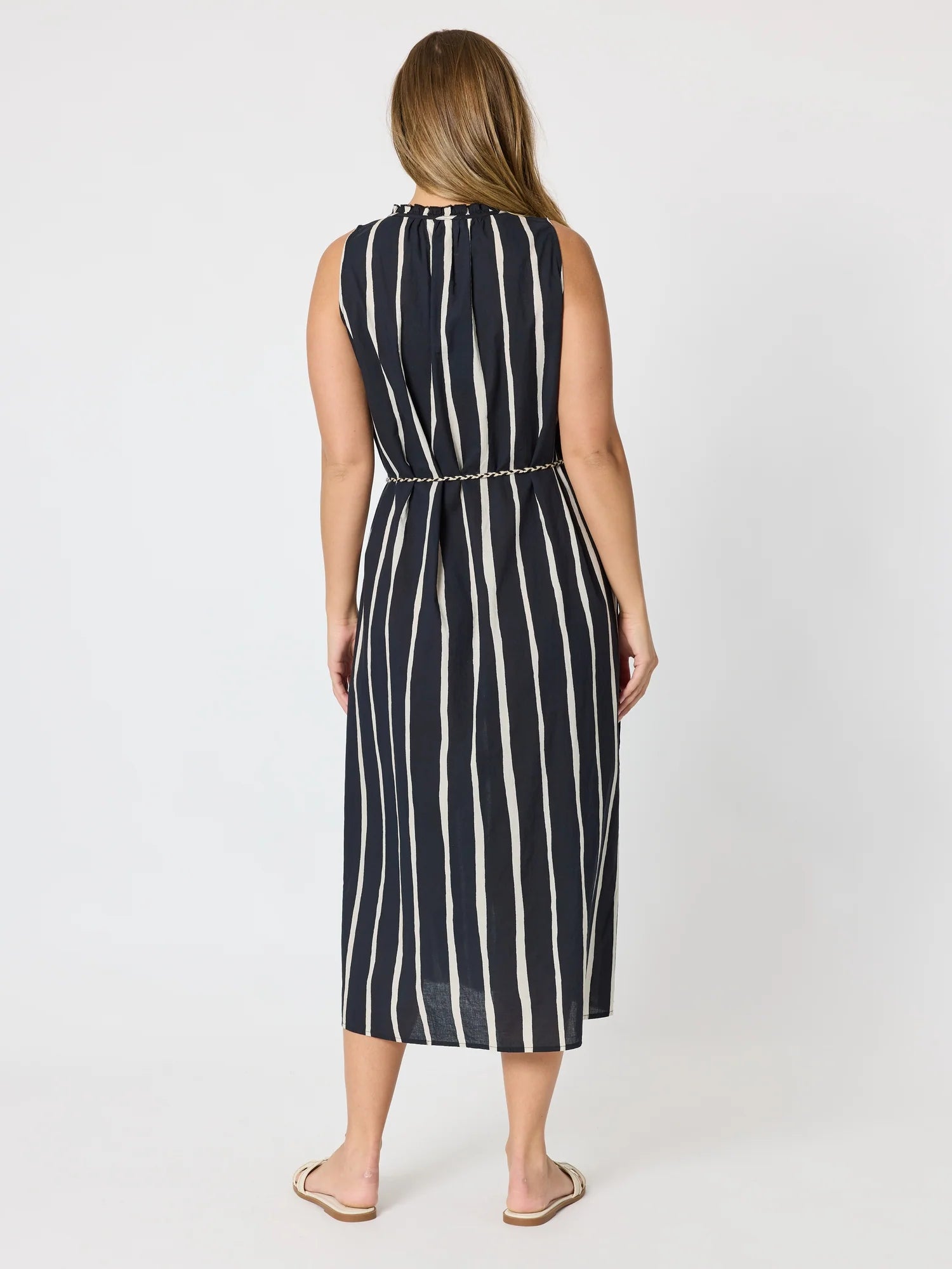 Image of A woman viewed from the back wearing a Threadz sleeveless midi dress with vertical navy and off-white stripes, standing against a plain light gray studio background.