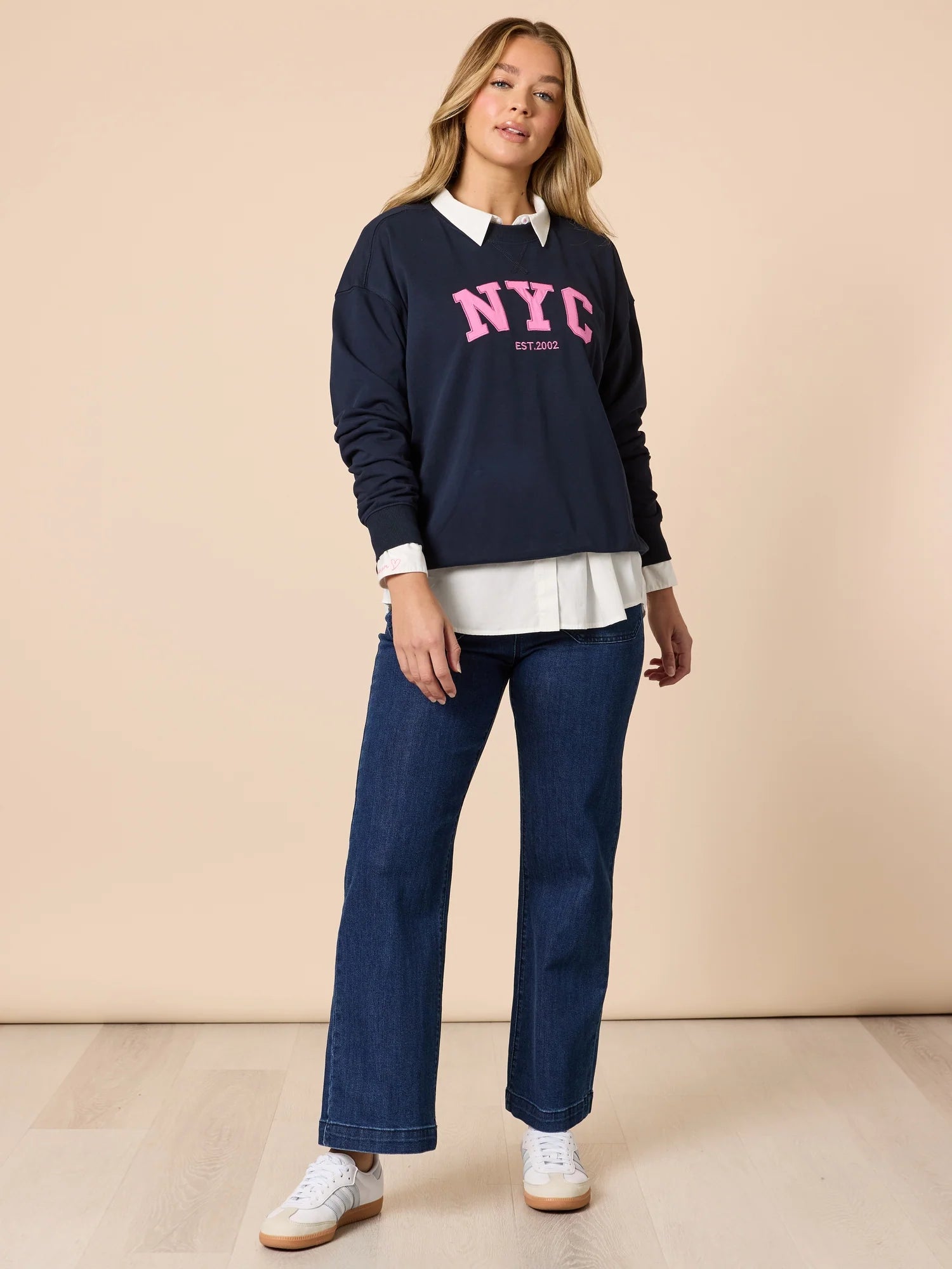 Collection of Woman wearing a navy sweatshirt with 'NYC' text, Threadz white shirt, and blue jeans on a beige background in a gallery layout