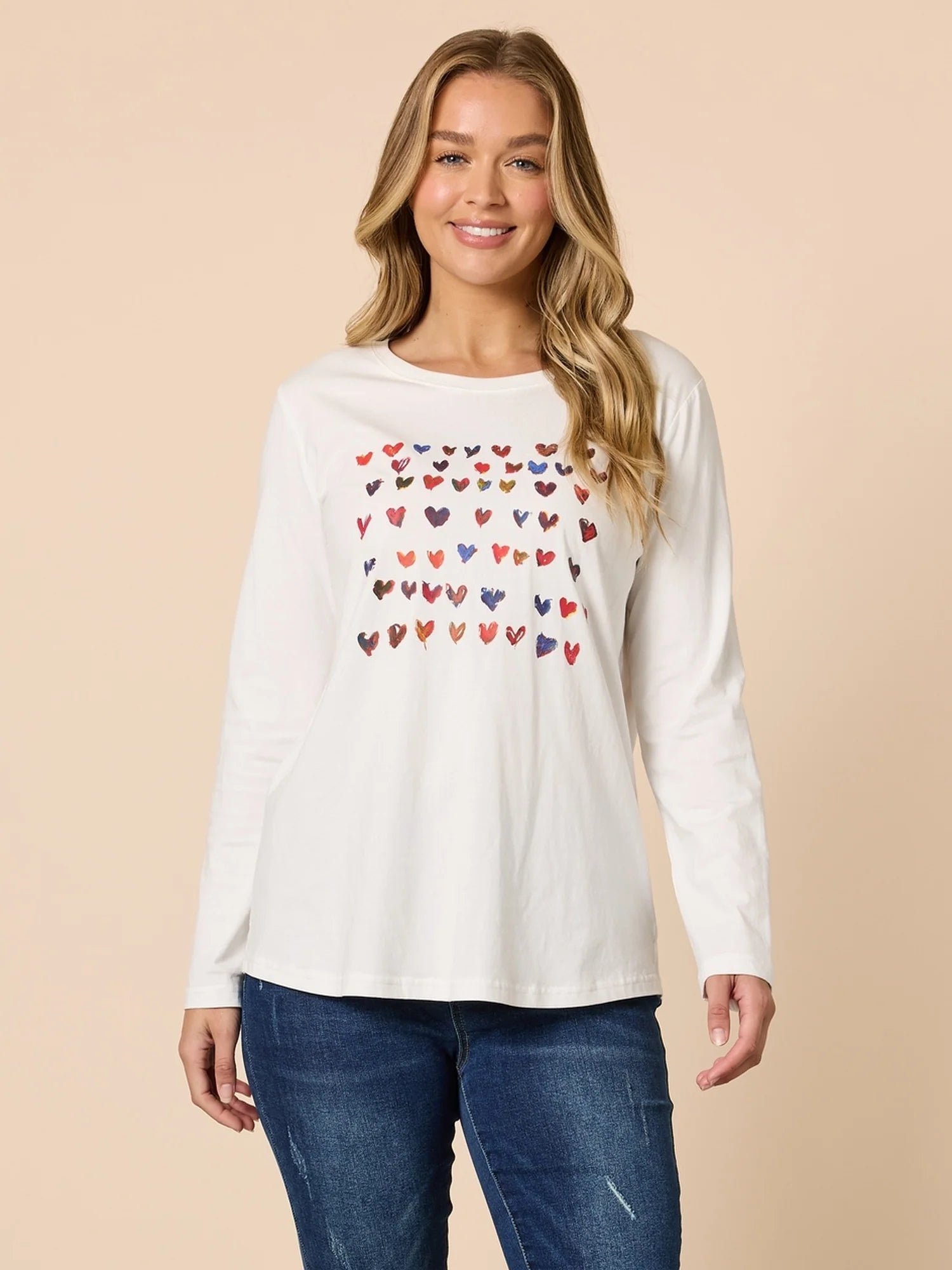 Woman wearing a Threadz white long-sleeve shirt with colorful heart pattern on a beige background