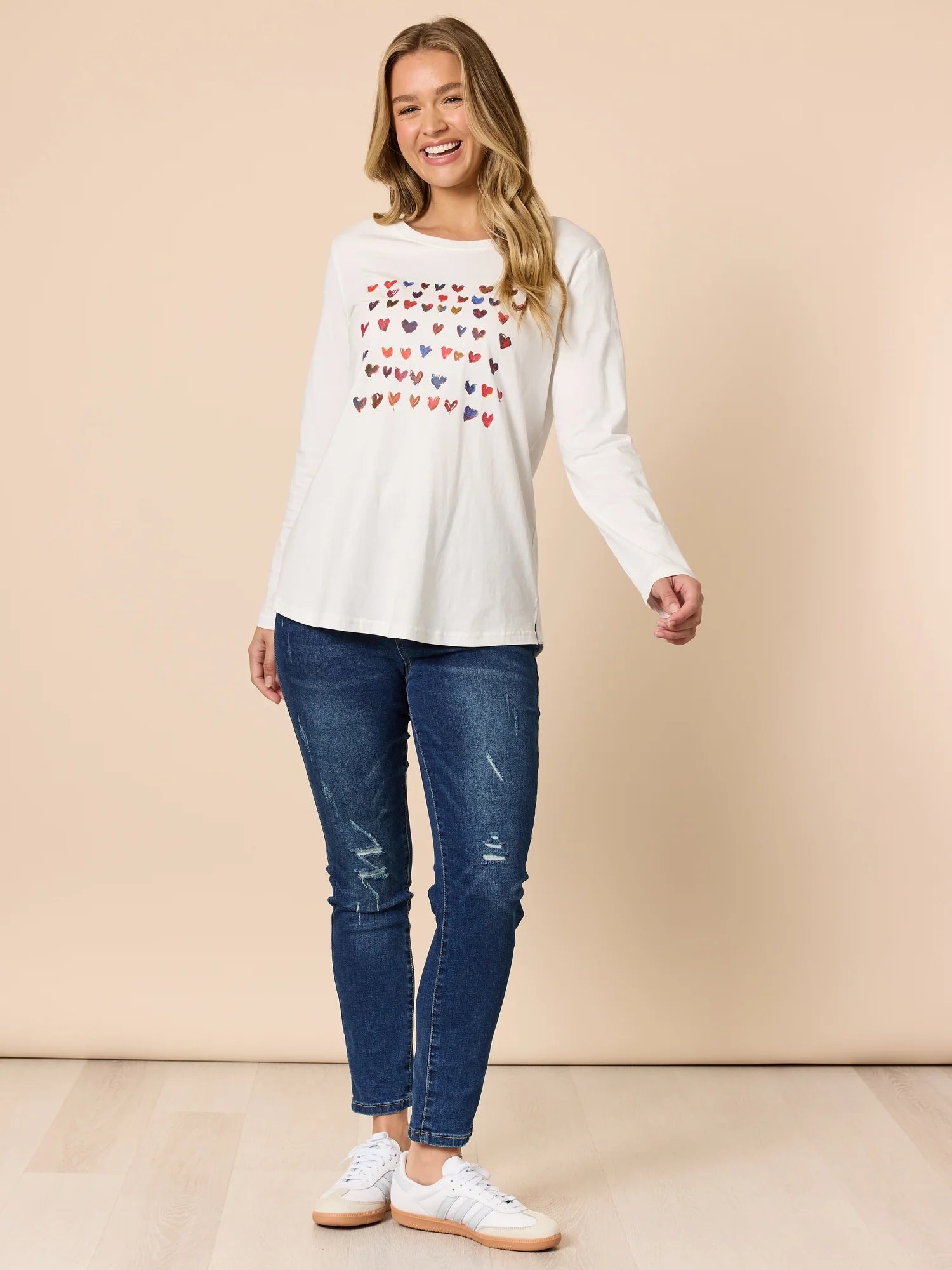 Collection of Woman wearing a Threadz white long-sleeve top with heart patterns and blue jeans on a beige background in a gallery layout