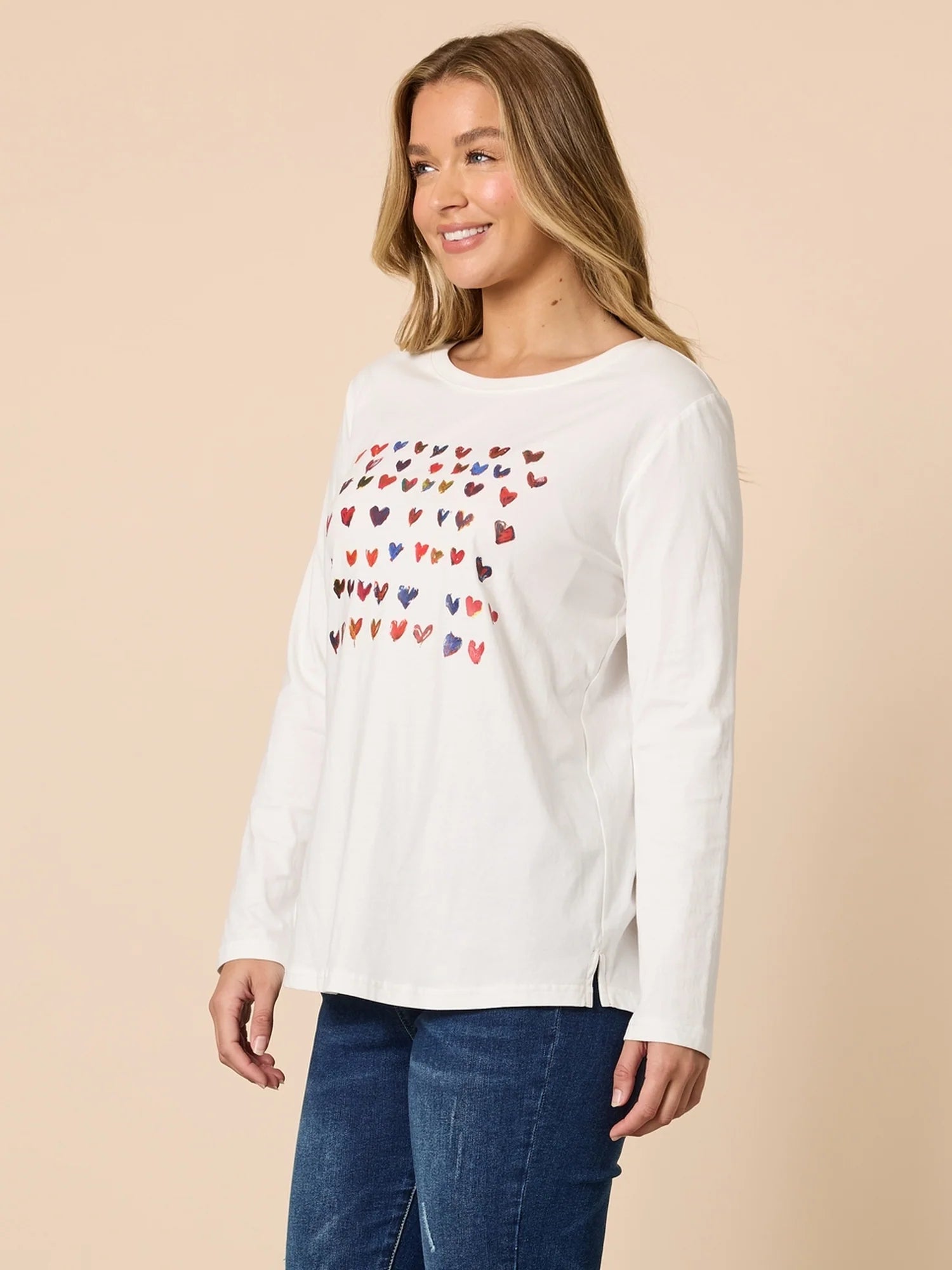 Woman wearing a Threadz white long-sleeve shirt with colorful heart pattern on a beige background