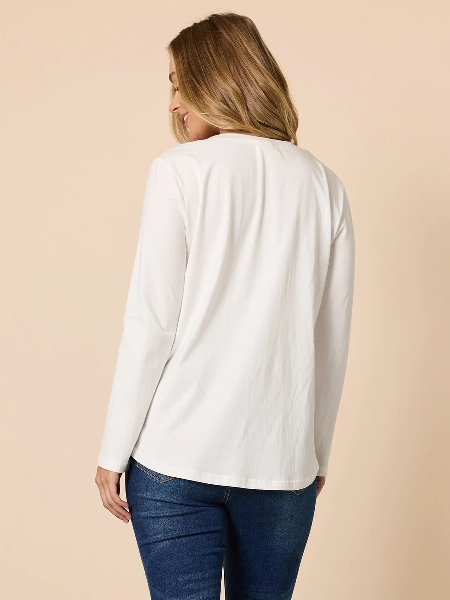 Woman wearing a Threadz white long-sleeve top and blue jeans on a beige background