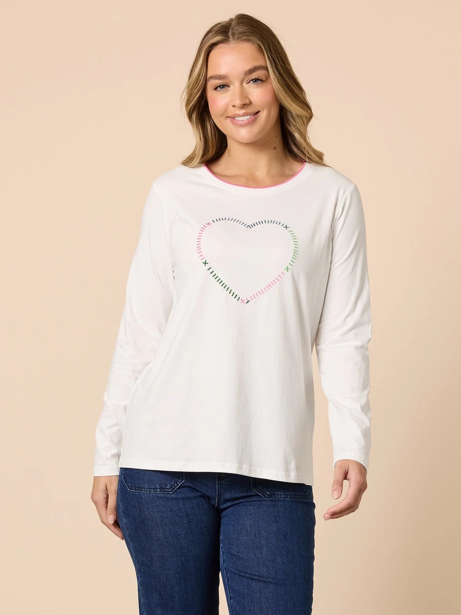Woman wearing a Threadz white long-sleeve shirt with a heart design on a beige background