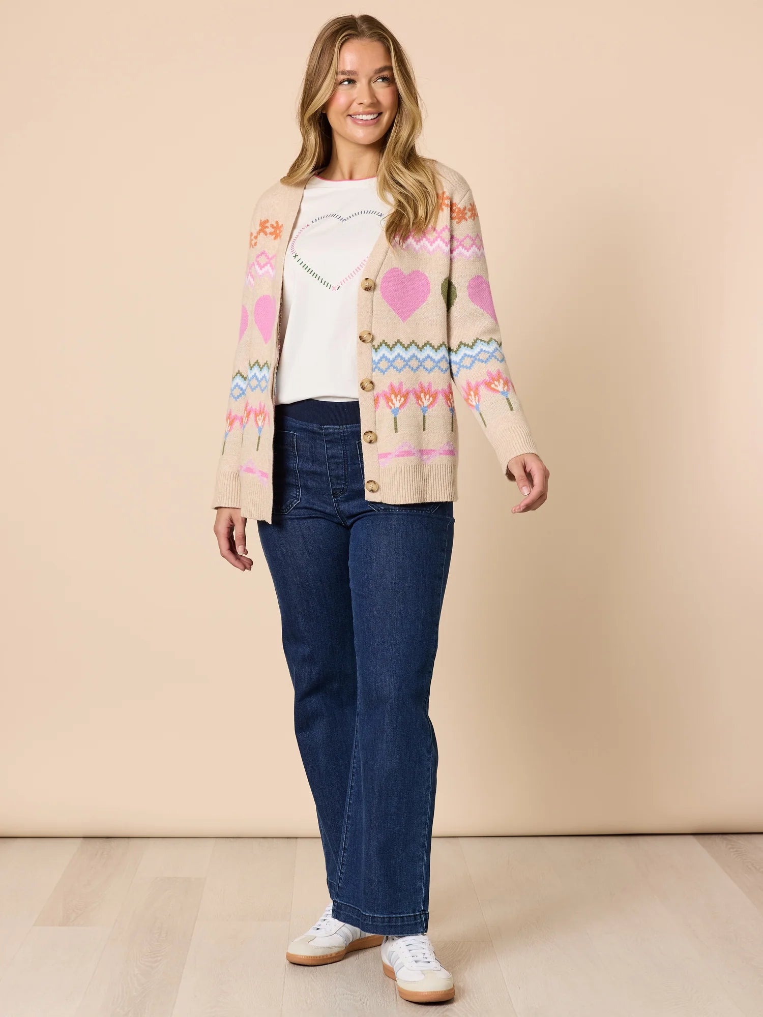 Image of Woman wearing a patterned cardigan, Threadz white shirt, blue jeans, and white sneakers on a beige background